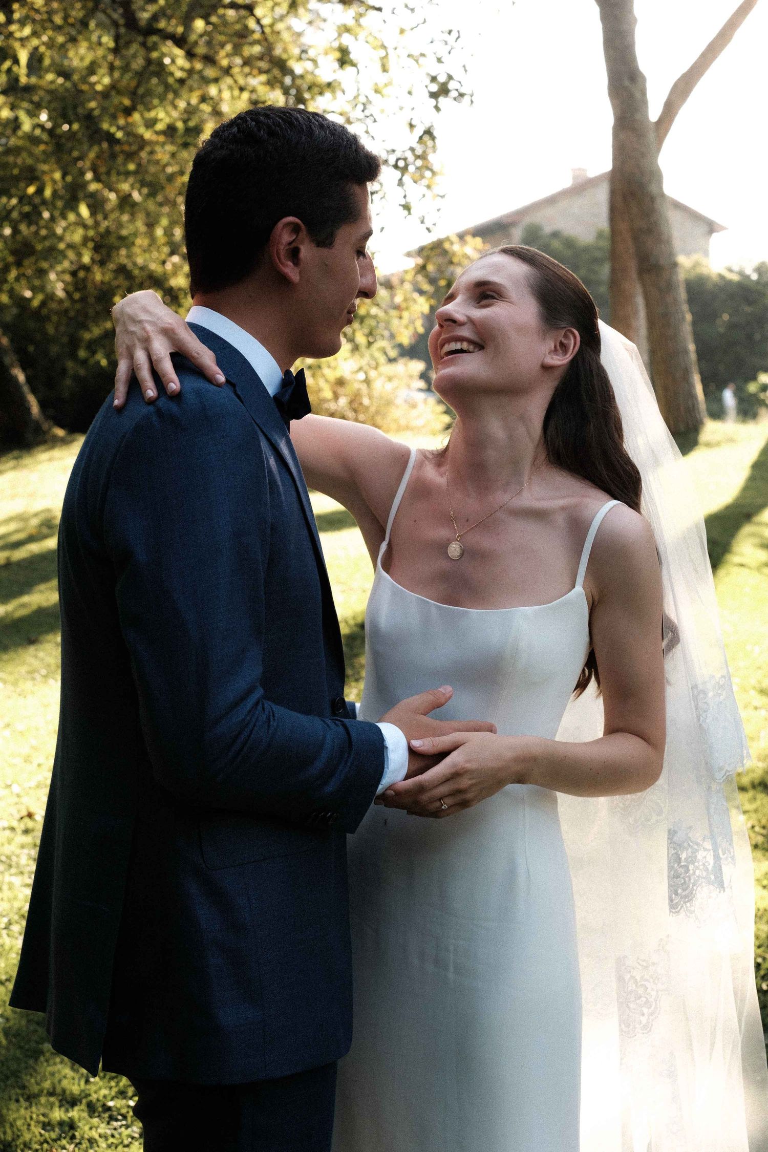A couple shares intimate moments in their wedding attire during a sunlit outdoor photoshoot.