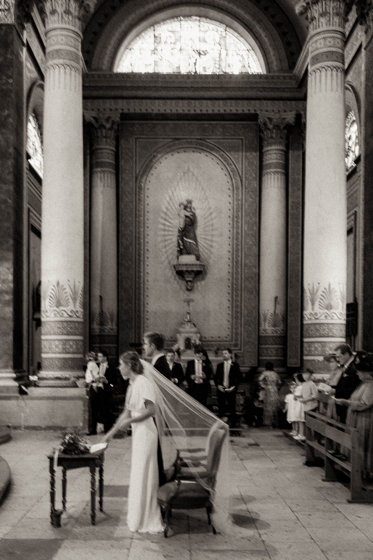 A vintage black and white photograph of a wedding ceremony inside an ornate church with tall columns and religious statues.