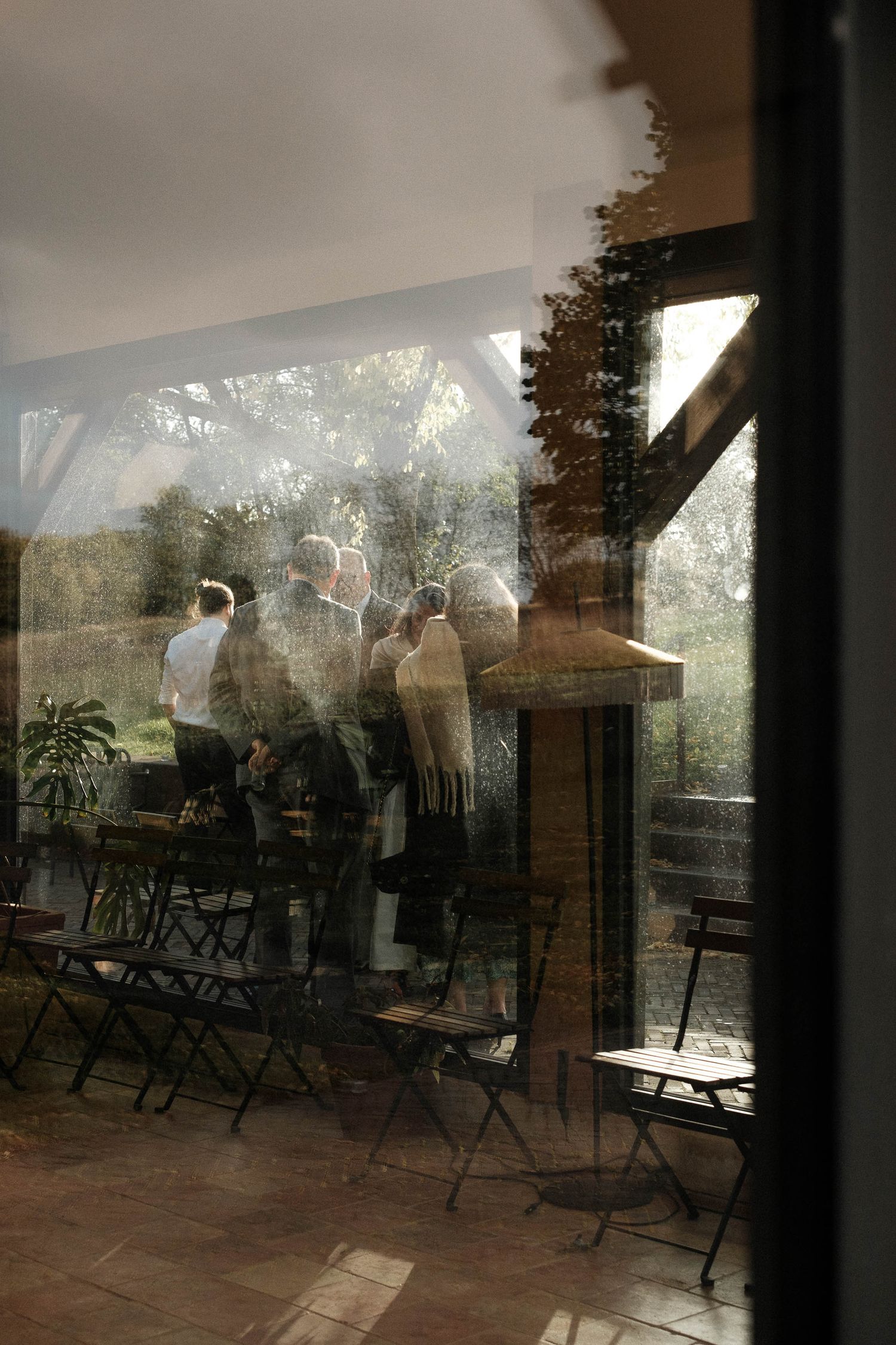 Silhouetted figures stand in a dimly lit room with folding chairs and sunlight streaming through large windows.