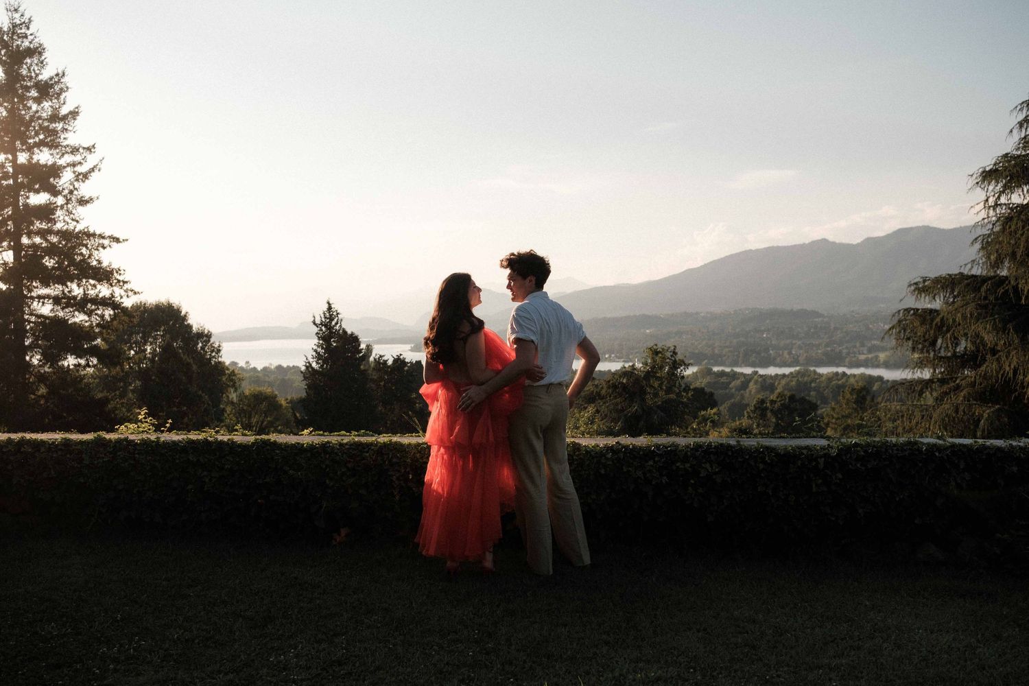 Silhouetted couple stands against sunset mountain backdrop in romantic scenic overlook setting.