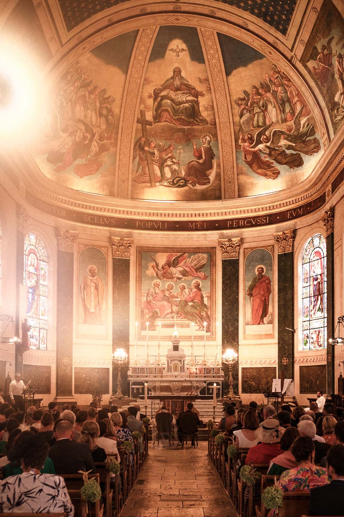 Interior panorama of a historic church with ornate frescoes and stained glass windows during a service.