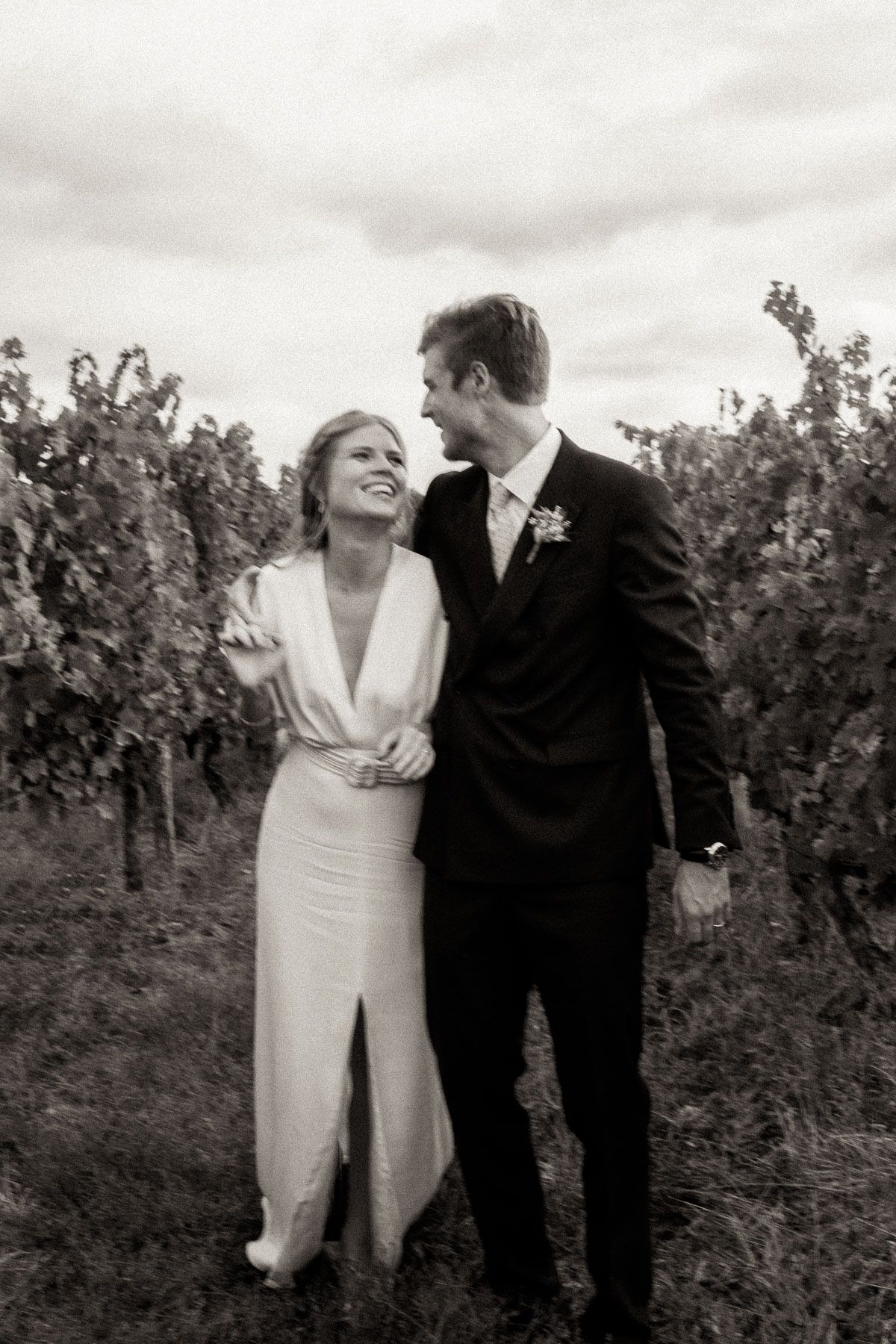 A romantic black and white wedding photo series showing a couple embracing among vineyard rows.