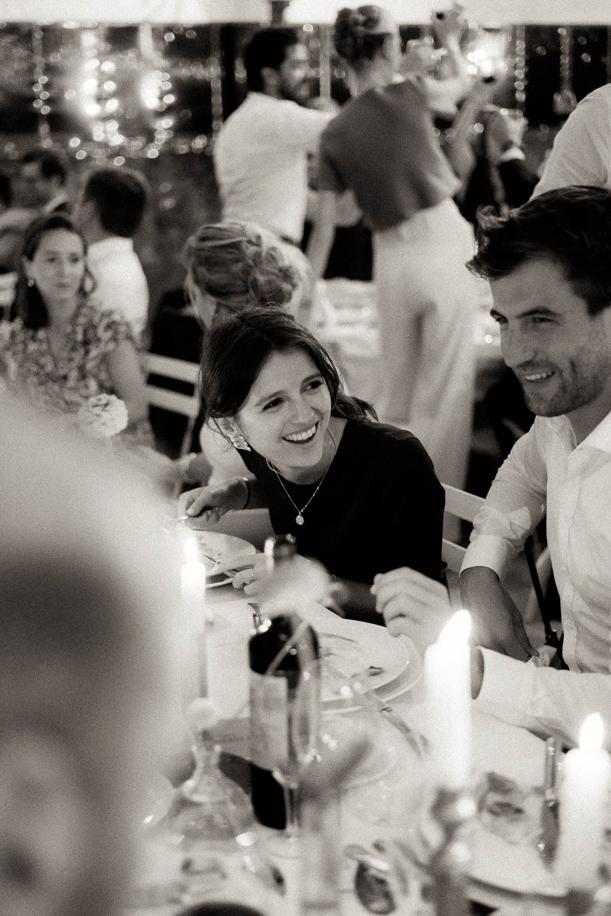 Black and white candid photo of guests laughing and enjoying themselves at a wedding reception dinner.