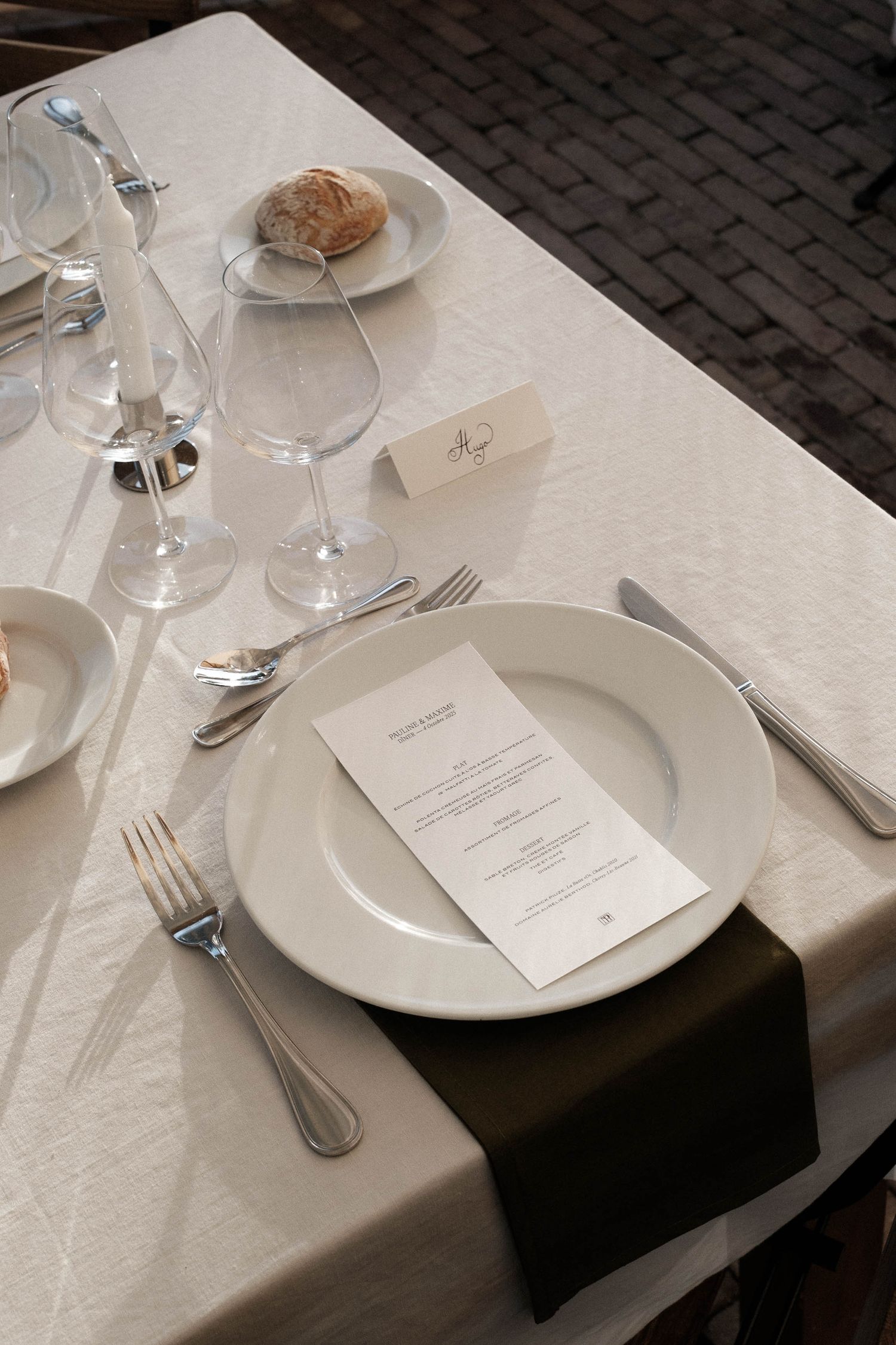 Elegant table setting with white plates, wine glasses, and menu card on crisp white tablecloth with black napkin.