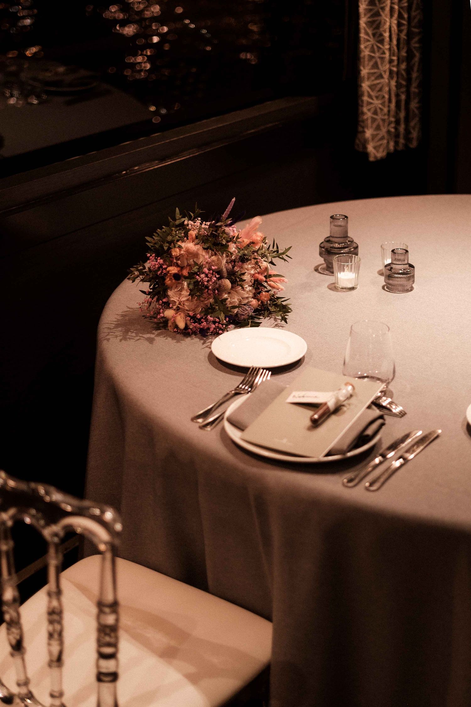 Elegant table settings with white linens and delicate floral arrangements in a dimly lit restaurant atmosphere.