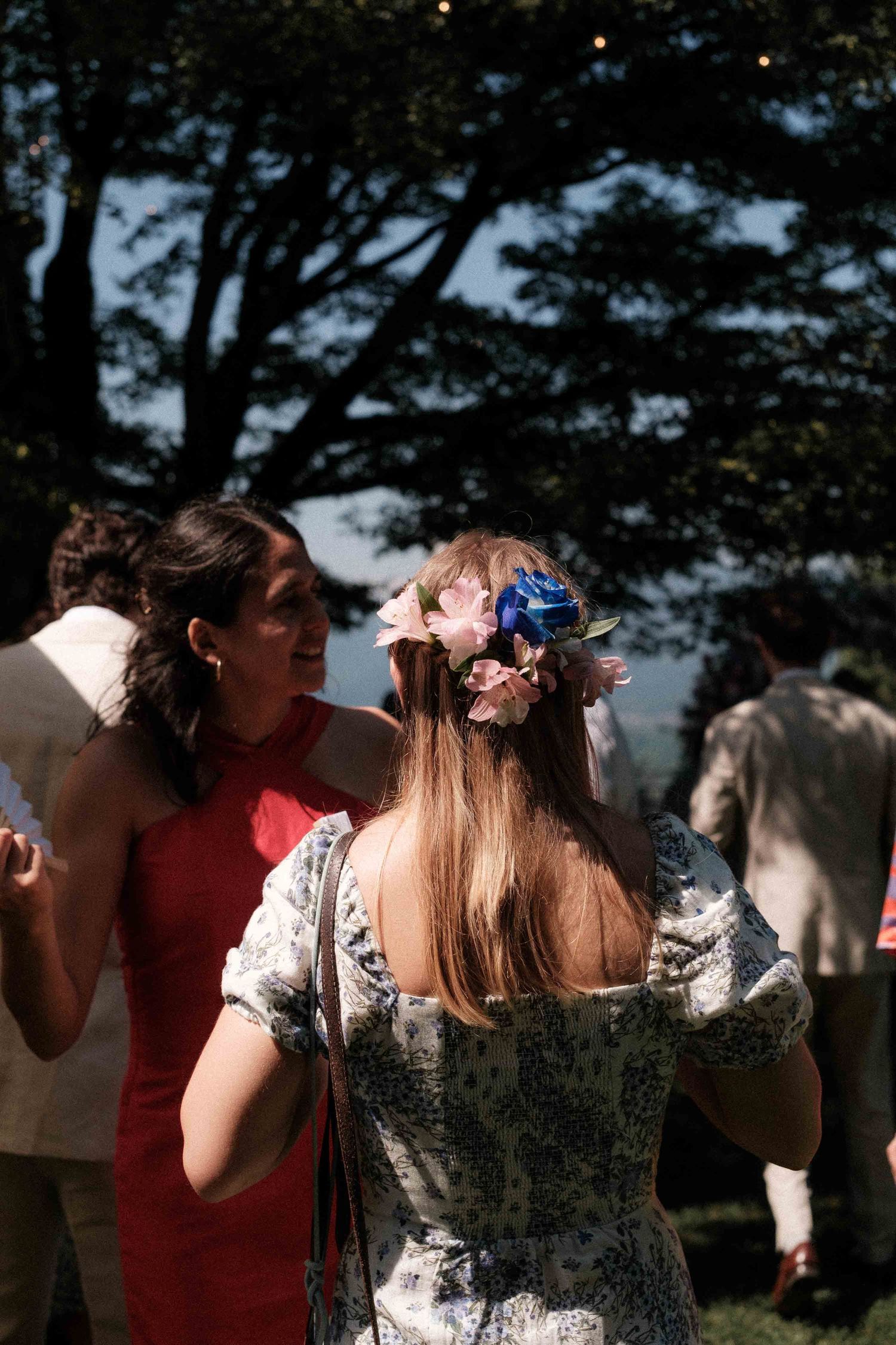 Guests at an outdoor summer celebration with a woman in a floral crown and vintage-style dress.