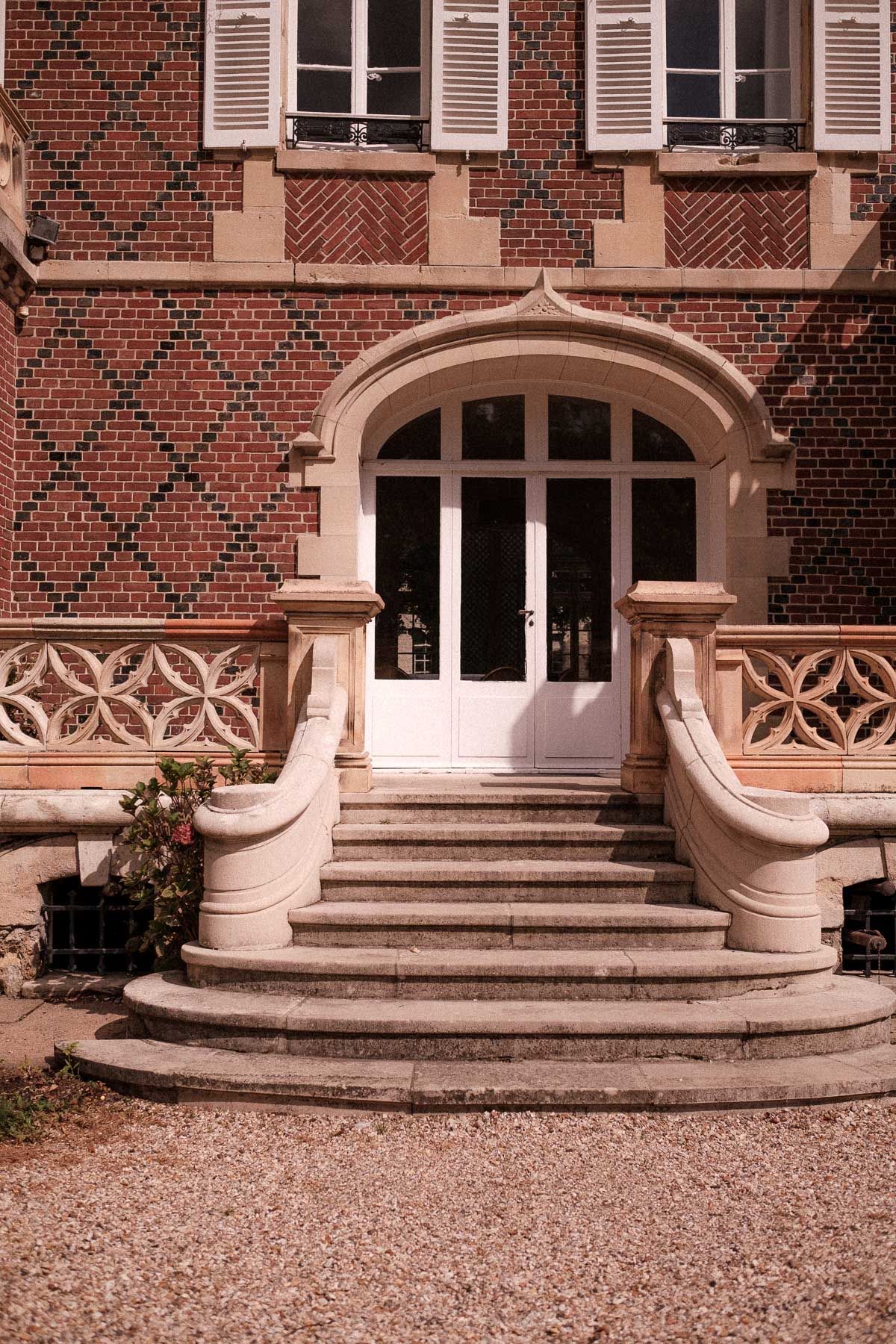Architectural detail of curved stone steps and ornate railings leading to entrance of historic brick building with white shutters.