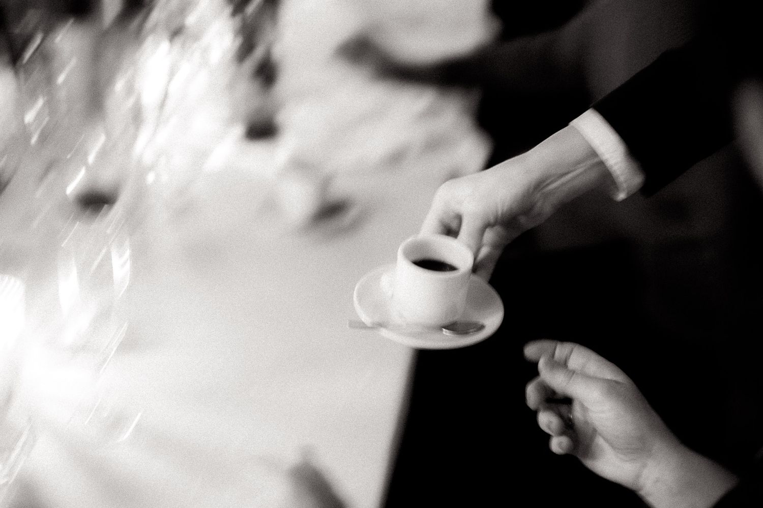 Hands pouring coffee or tea into a white cup in black and white artistic photography.
