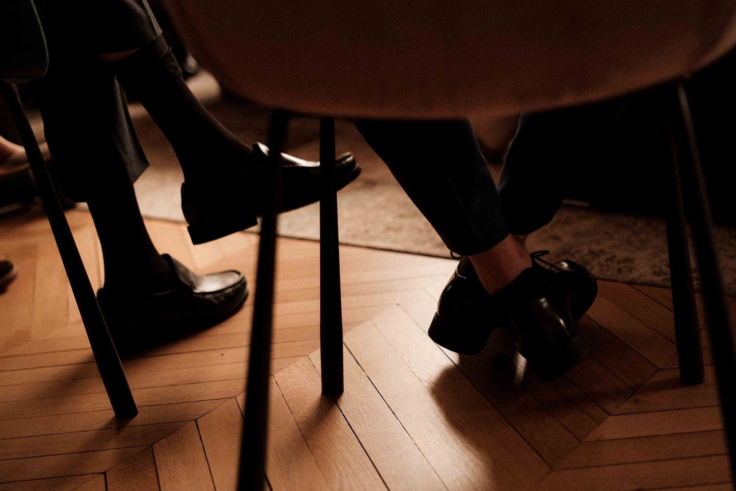 Low angle view of formal dress shoes and feet on a wooden dance floor in warm lighting.