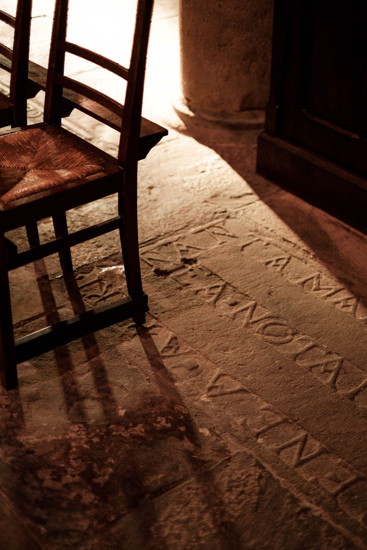 Ancient stone floor with carved Latin text illuminated by dramatic shadows from window bars in sepia tones.