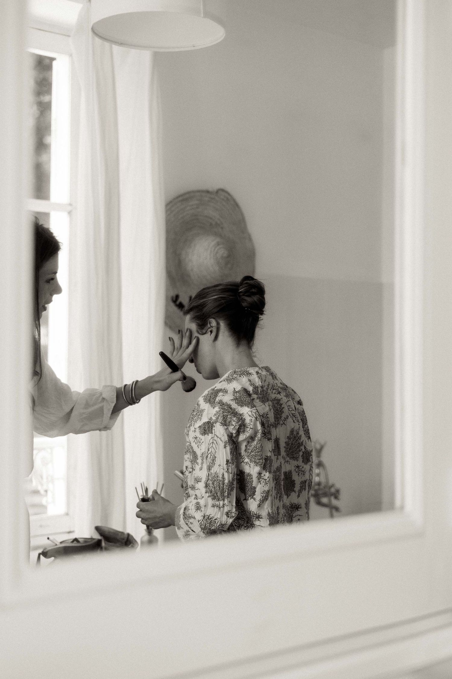 A series of four black and white photos showing people reflected in mirrors applying makeup in a dressing room.