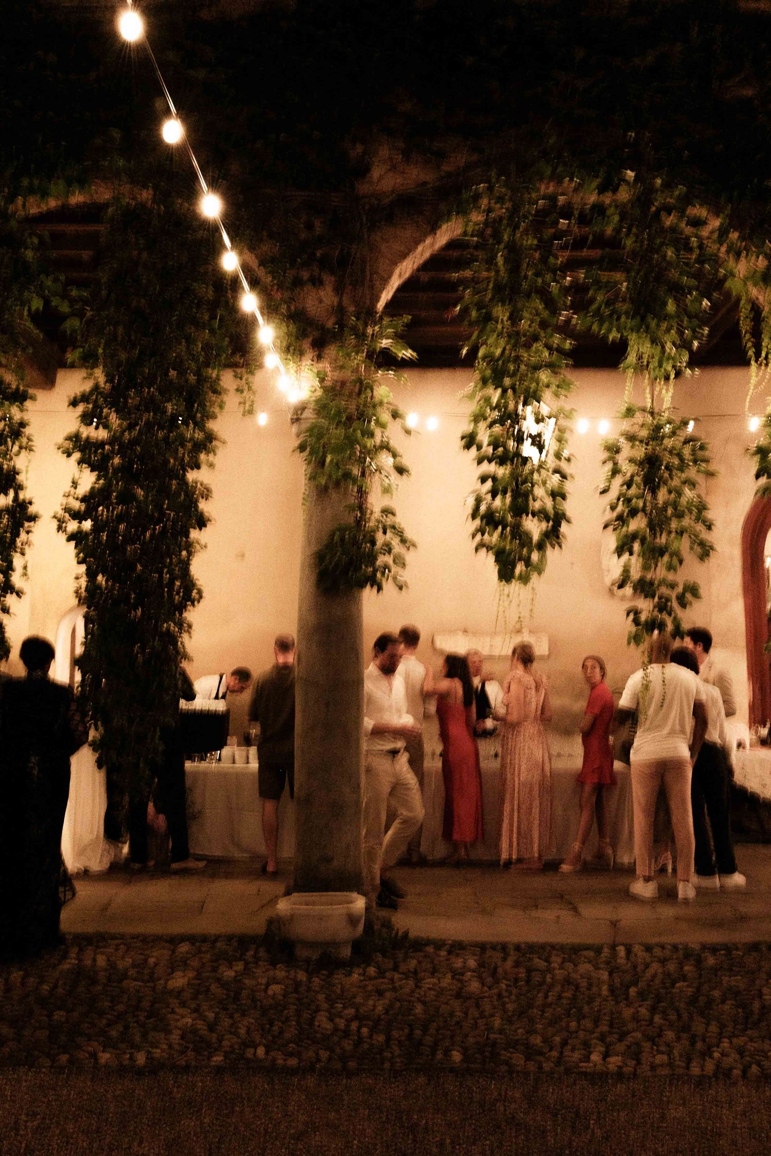 A row of people stand in white clothing under string lights at a nighttime outdoor gathering.