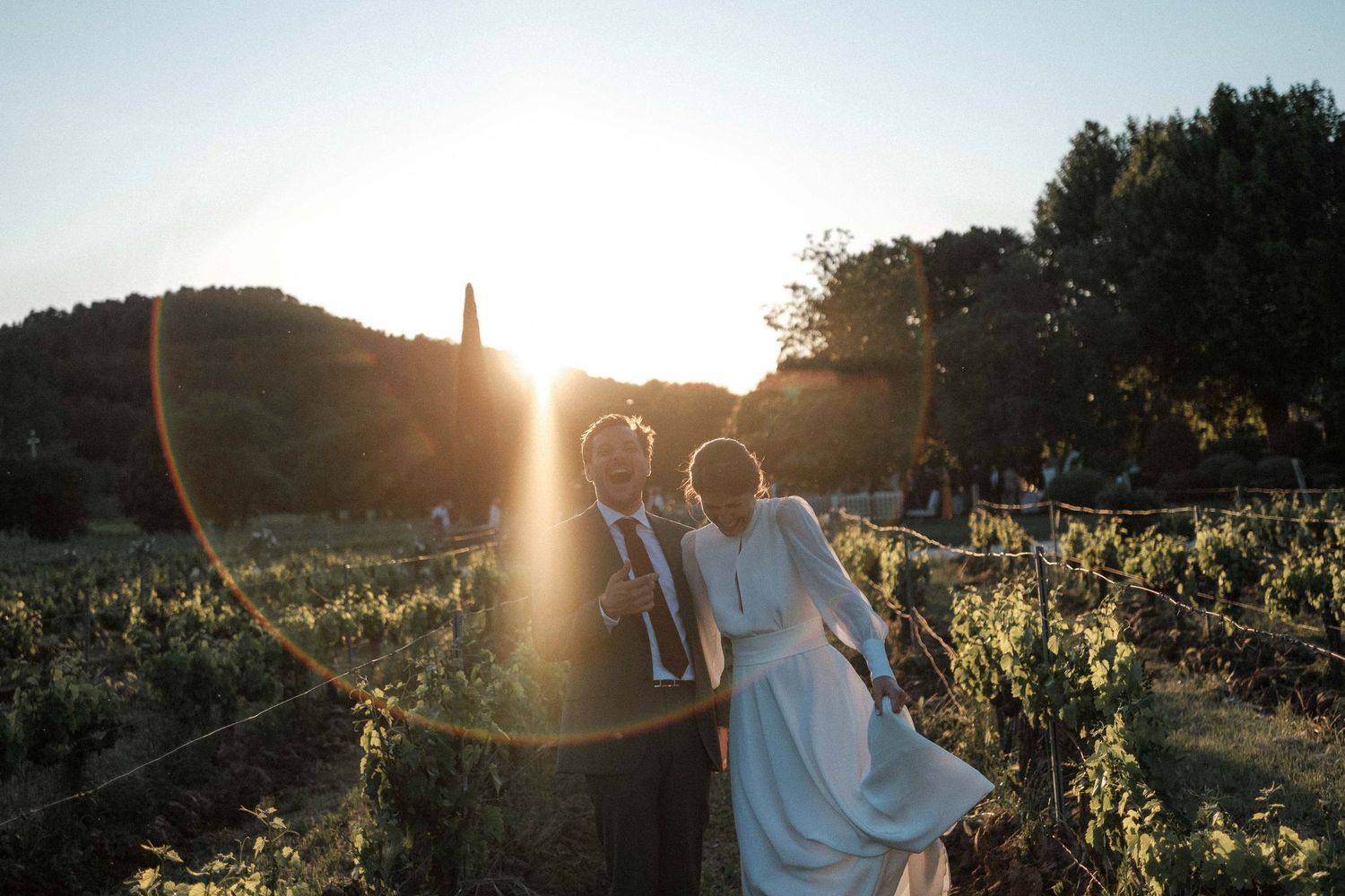Silhouetted couple embraces in a sunlit sunflower field at golden hour creating a romantic summer scene.