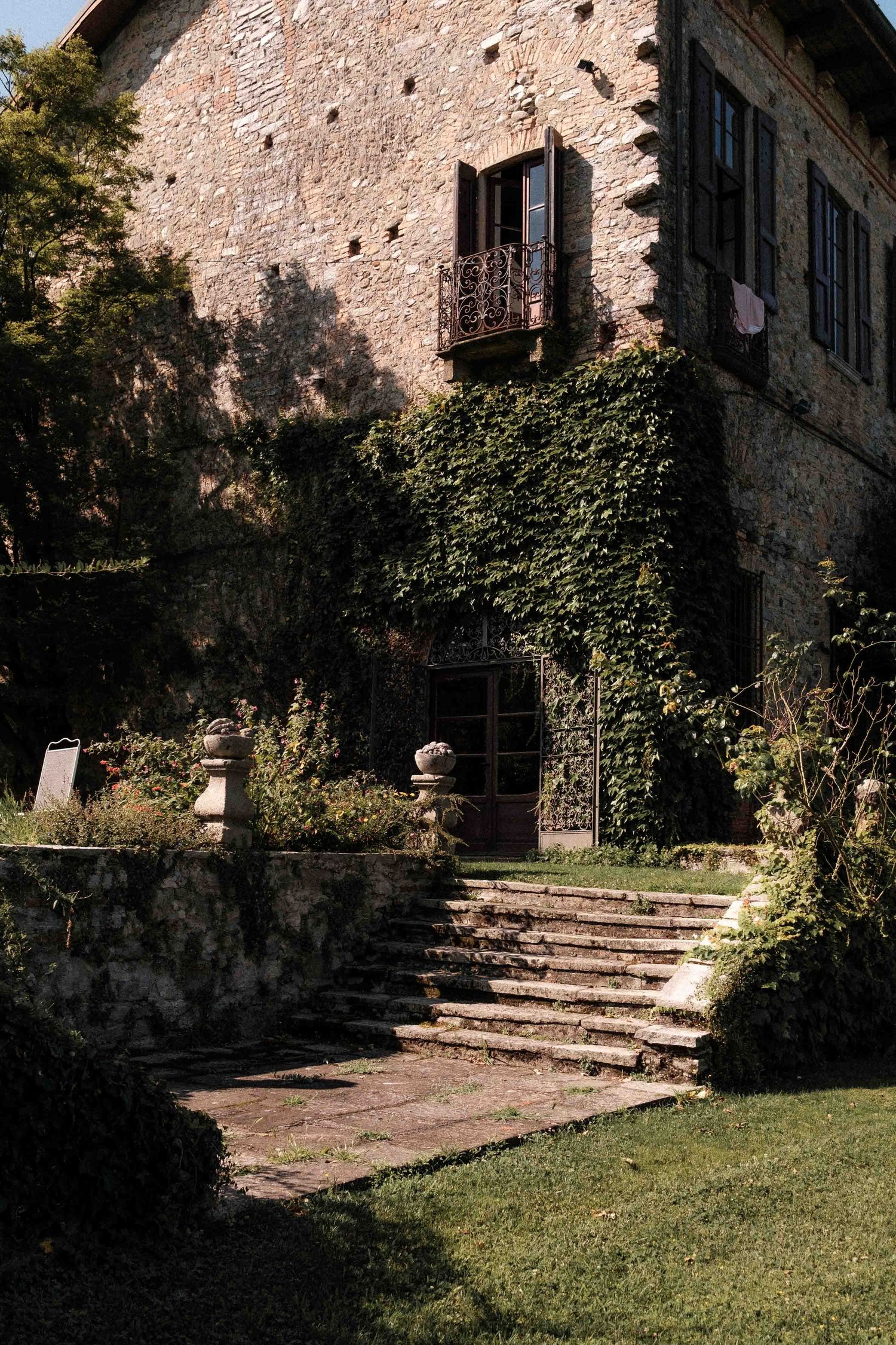 Stone steps lead up to a rustic building entrance with ivy-covered walls and a well-maintained green lawn.