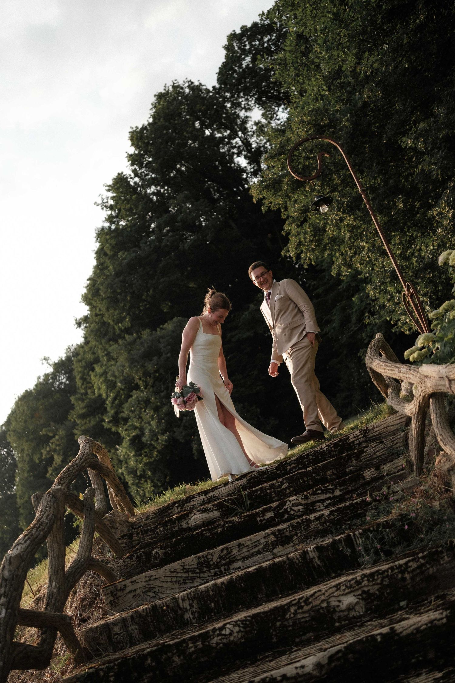 A couple climbs on a fallen tree trunk in a romantic outdoor photoshoot at dusk.