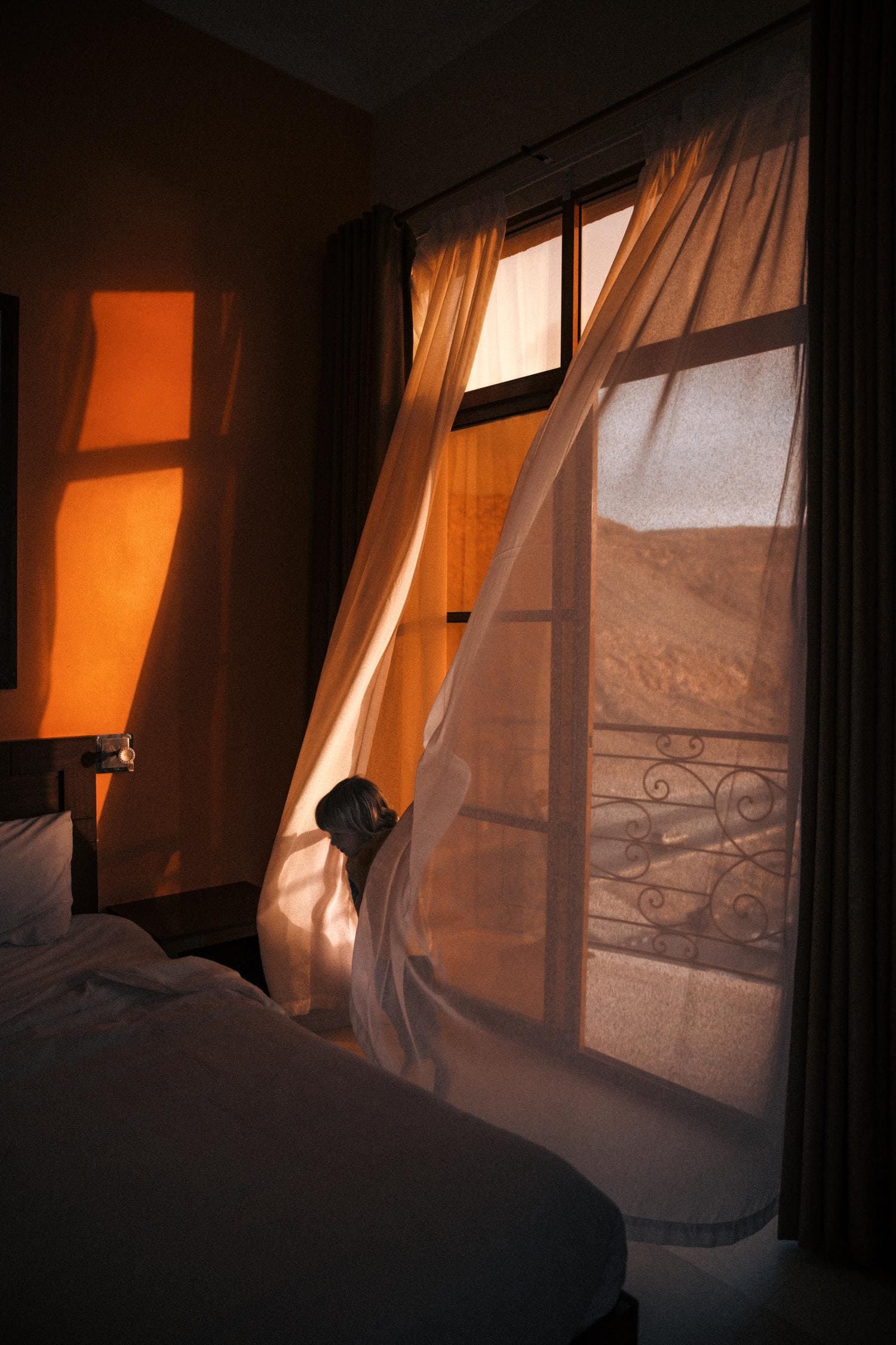 Curtains billow in warm sunlight through multiple windows creating a dreamy, ethereal atmosphere in a dimly lit room.