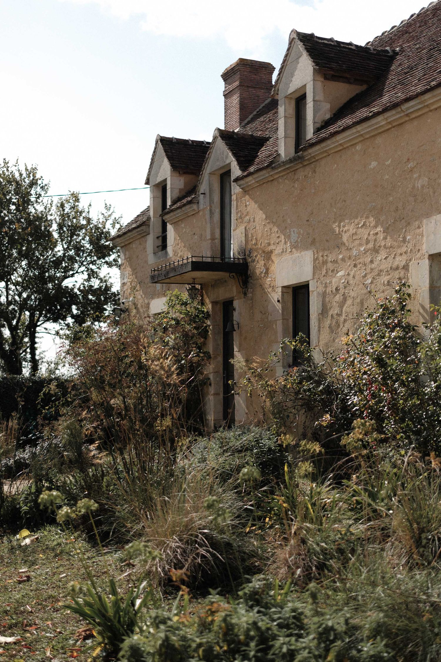 Rustic stone farmhouses with steep roofs line a grassy hillside in the French countryside.