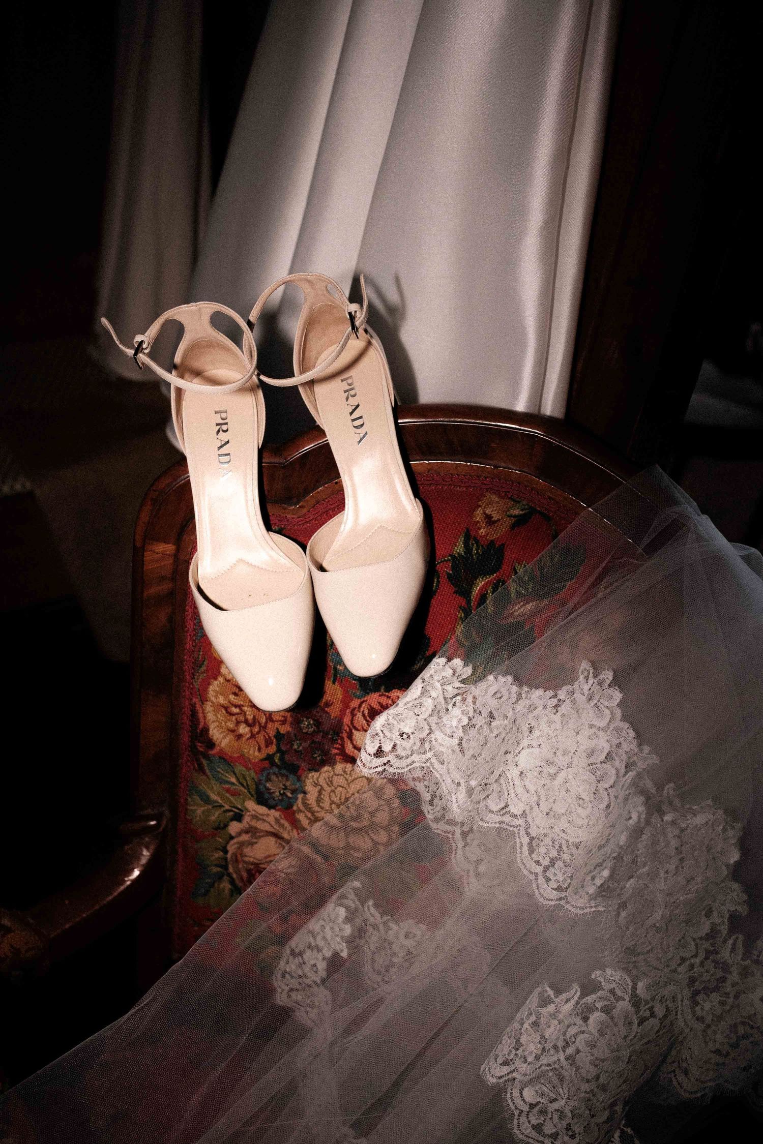 White bridal shoes displayed with delicate lace fabric in dramatic lighting creating an artistic wedding detail shot.