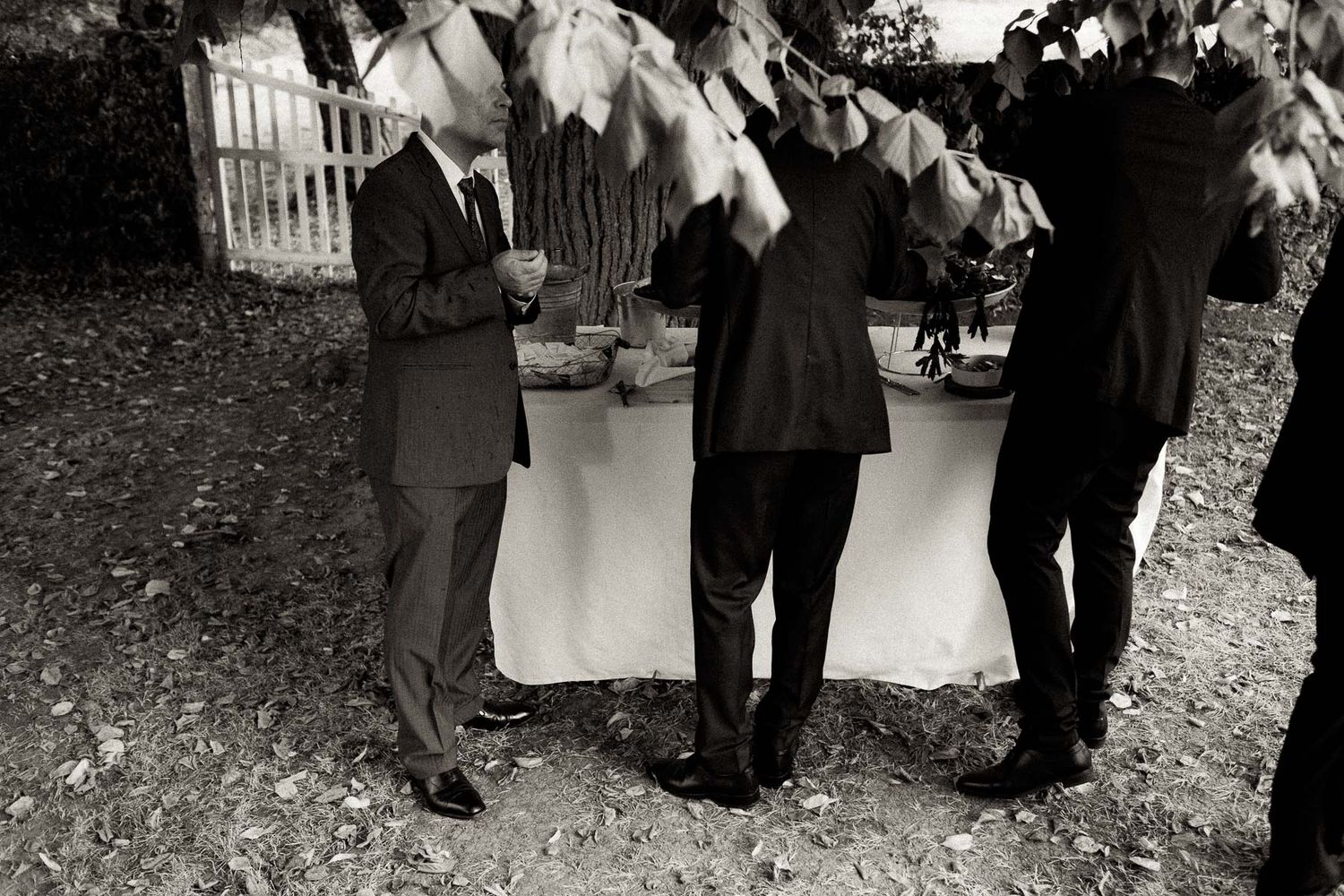 Three people in dark suits stand together at an outdoor event in a black and white photograph.