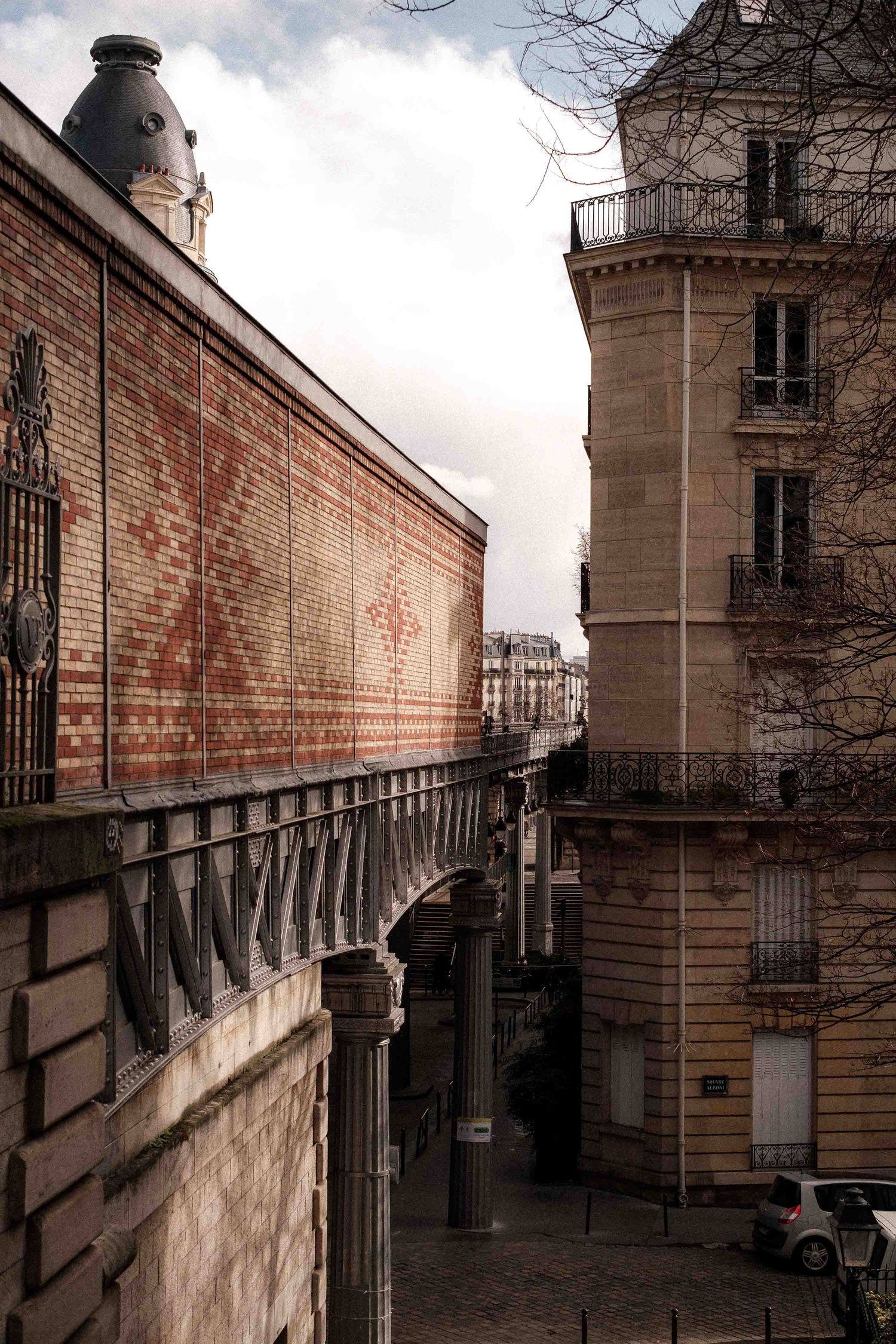 Brick walls and wrought iron railings line a narrow walkway at a historic building complex in Paris.