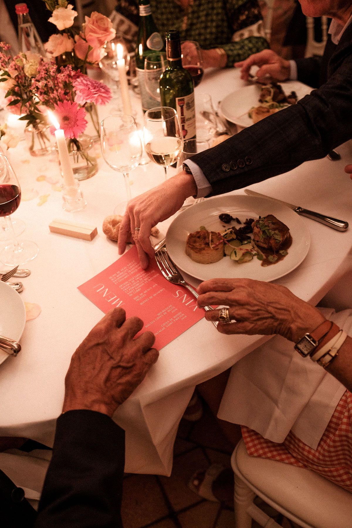 Hands holding napkins at an elegant dinner table setting with soft pink lighting and floral centerpieces.