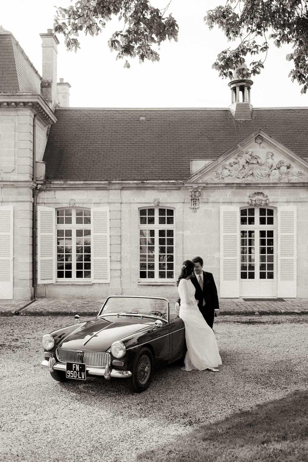Vintage MG sports car parked in front of an elegant French chateau with classical architecture.