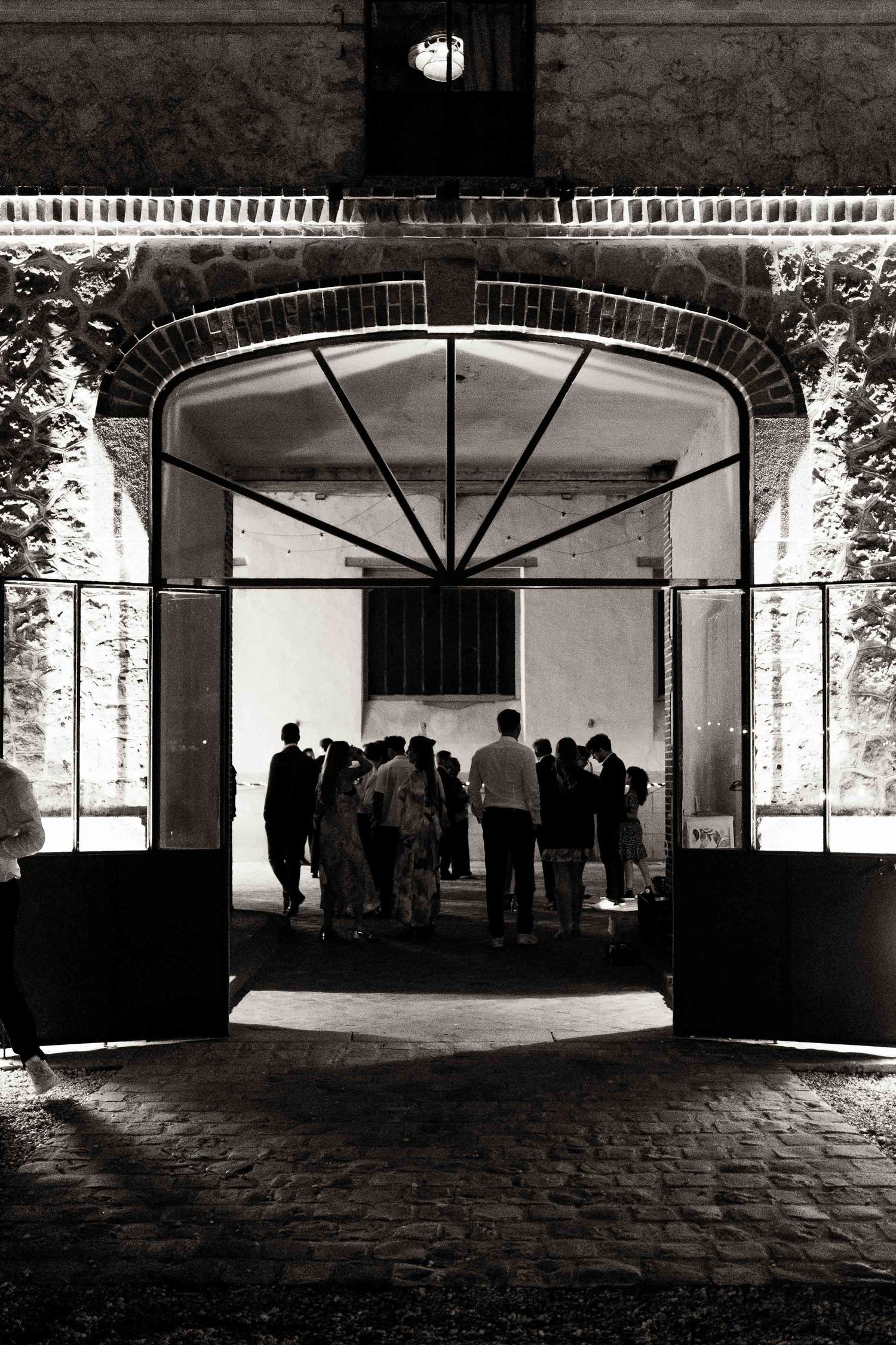 Silhouetted figures stand in a dark archway with sunlit windows creating a dramatic architectural interior space.