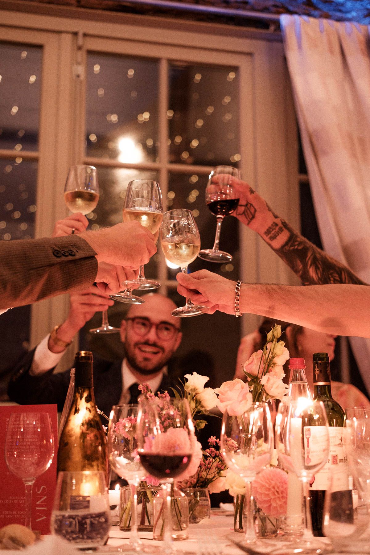 People raise wine glasses in a toast at an elegant candlelit dinner table decorated for a celebration.