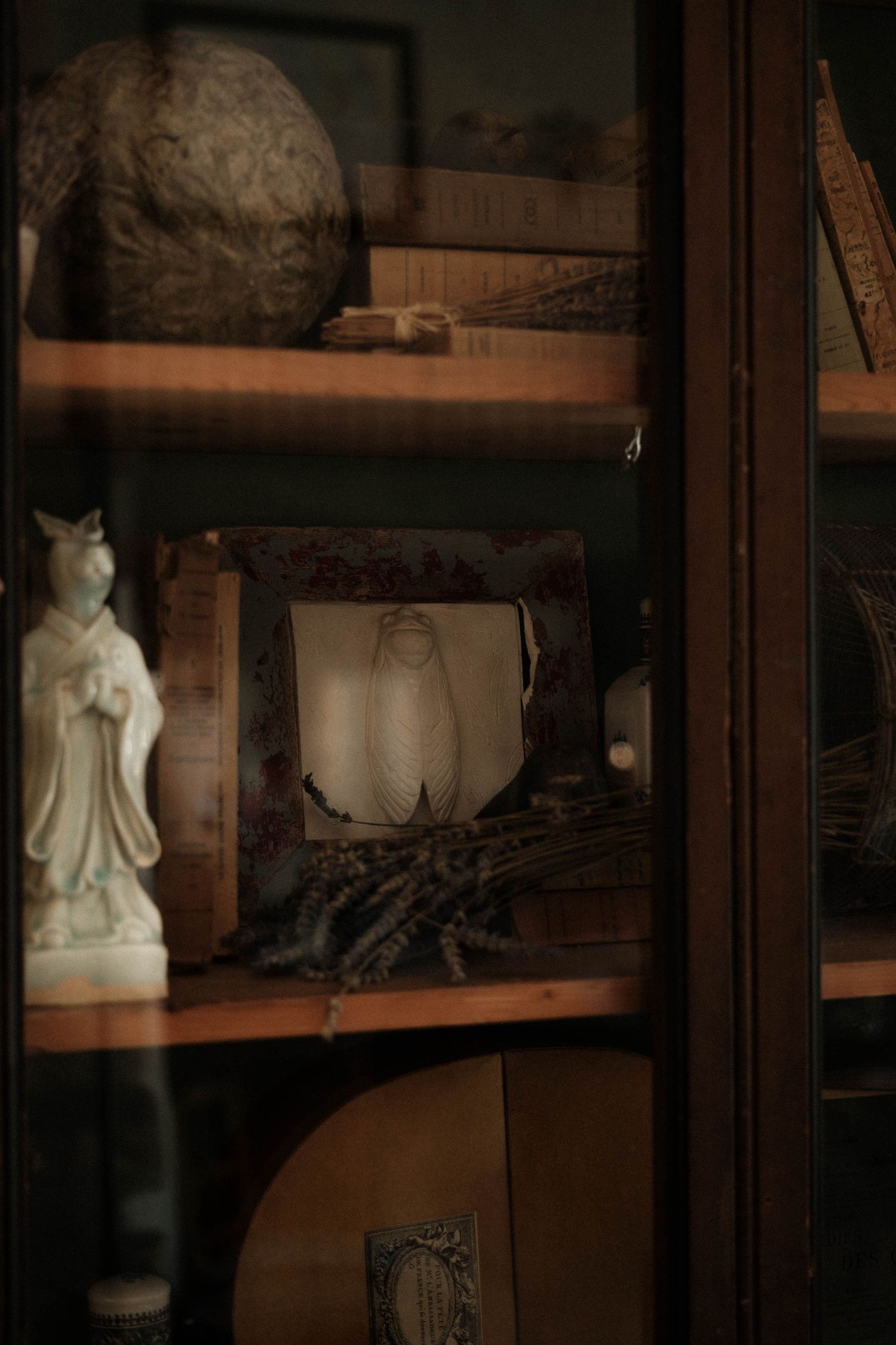 Antique glass cabinet displays decorative white porcelain figurines and collectibles on wooden shelves.