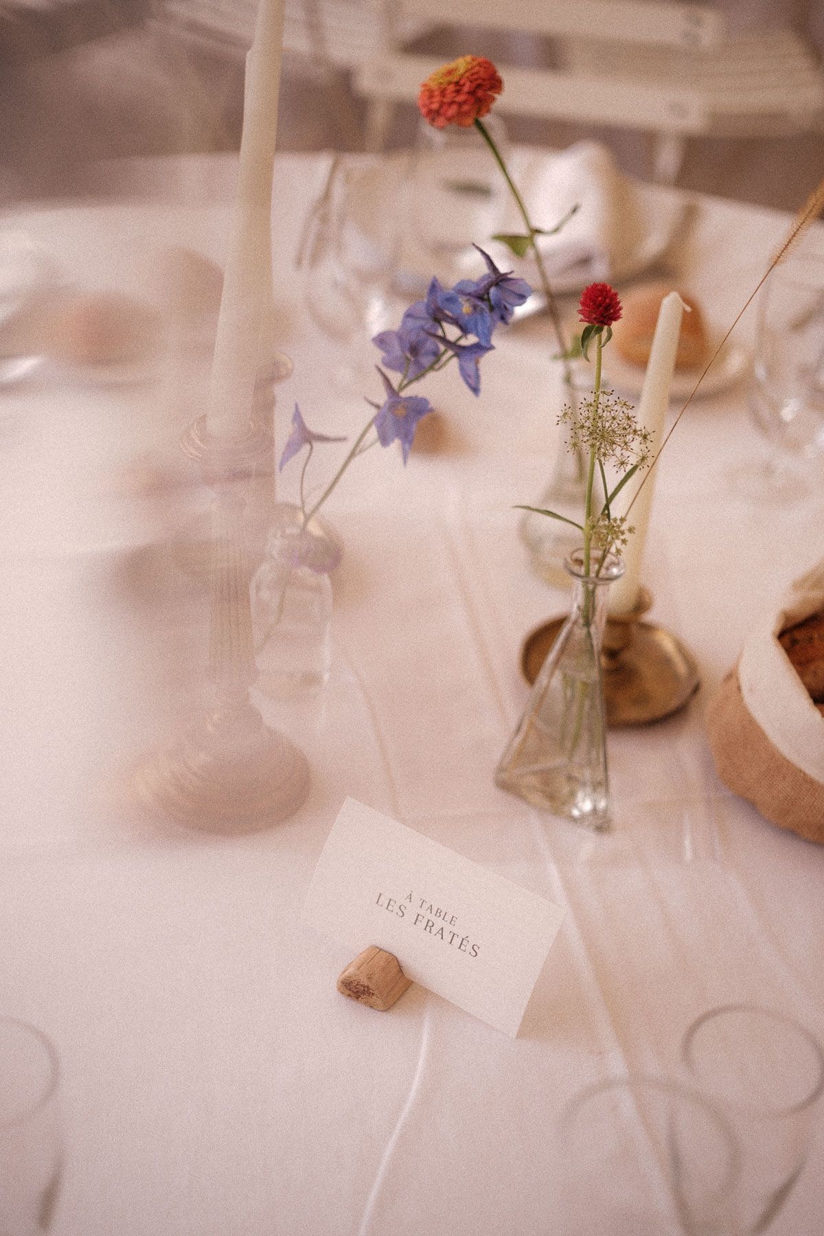Elegant table setting with delicate flowers in small vases and place cards on a white tablecloth.