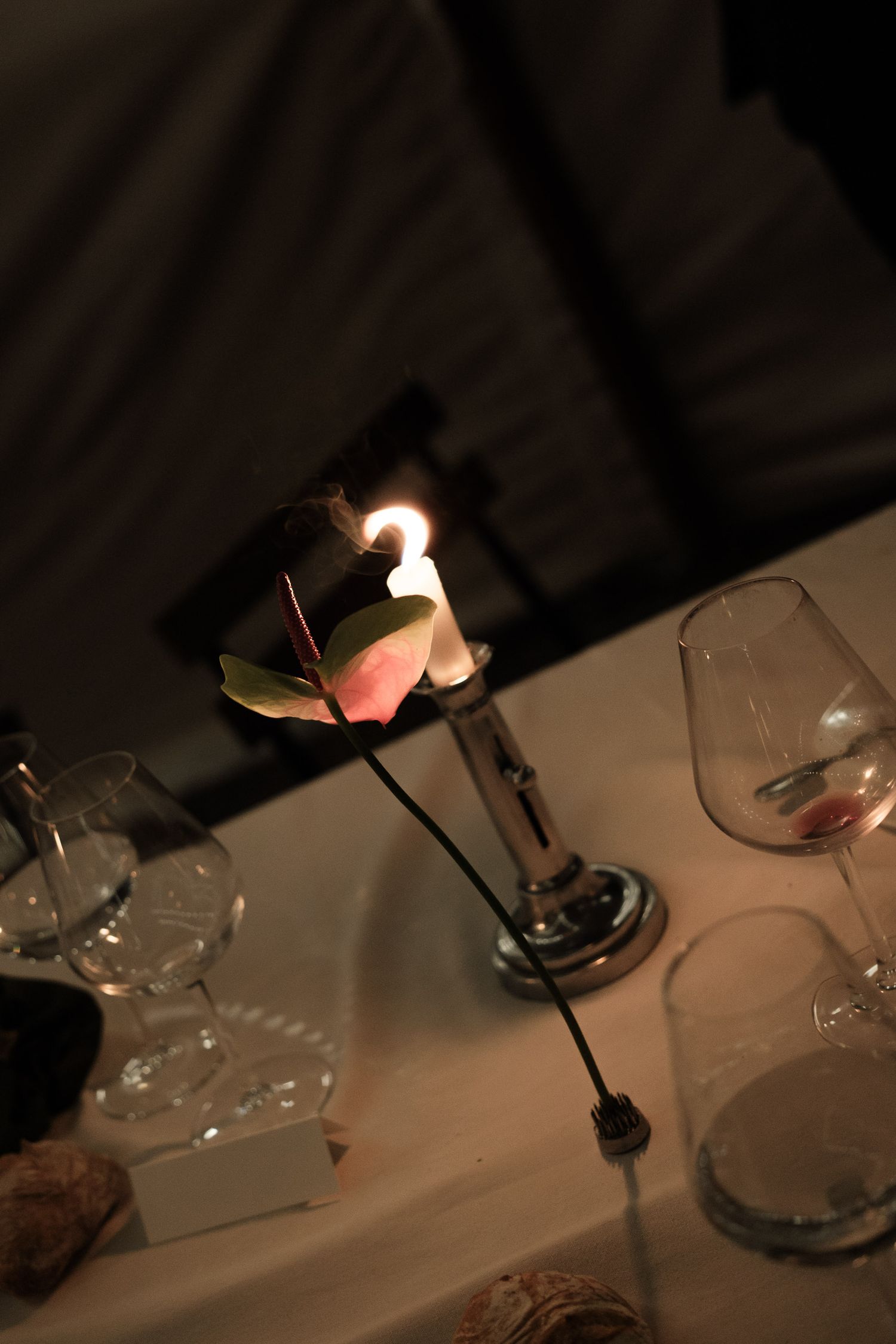 Candlelit table setting in a dimly lit restaurant with elegant glassware and white tablecloth.