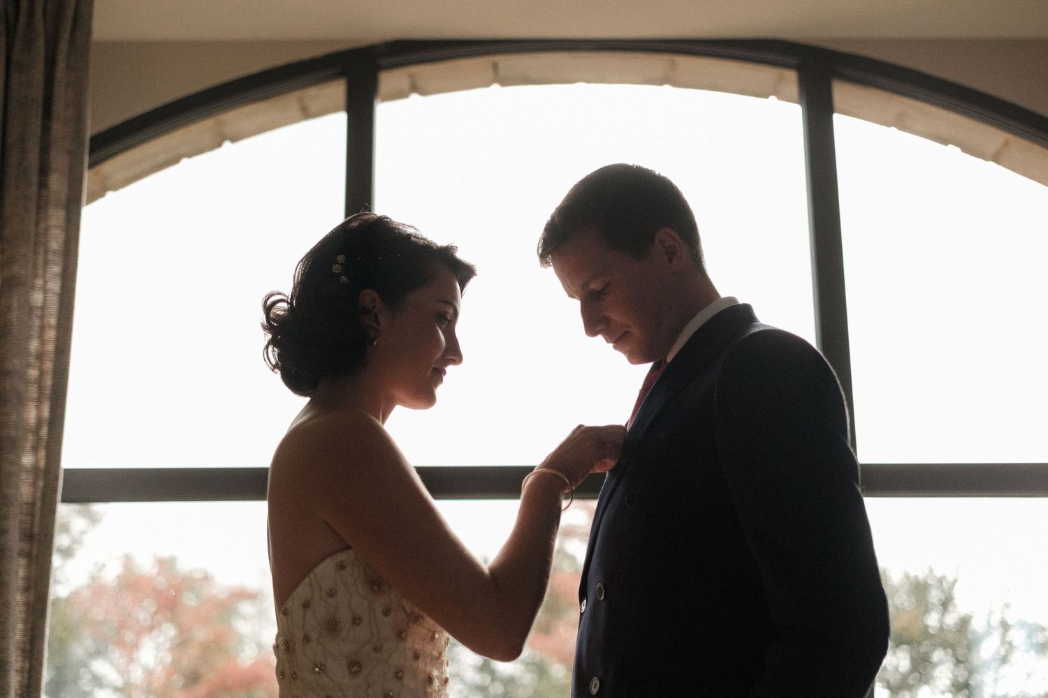 Wedding party silhouettes stand against large arched windows during an elegant indoor reception.