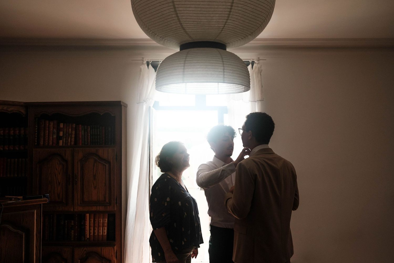 Silhouettes of figures stand in a dimly lit room with dramatic backlighting creating a moody atmosphere.