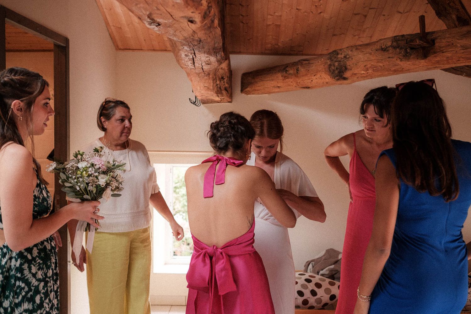 A group of people in colorful dresses prepare for a formal event in a sunlit room.