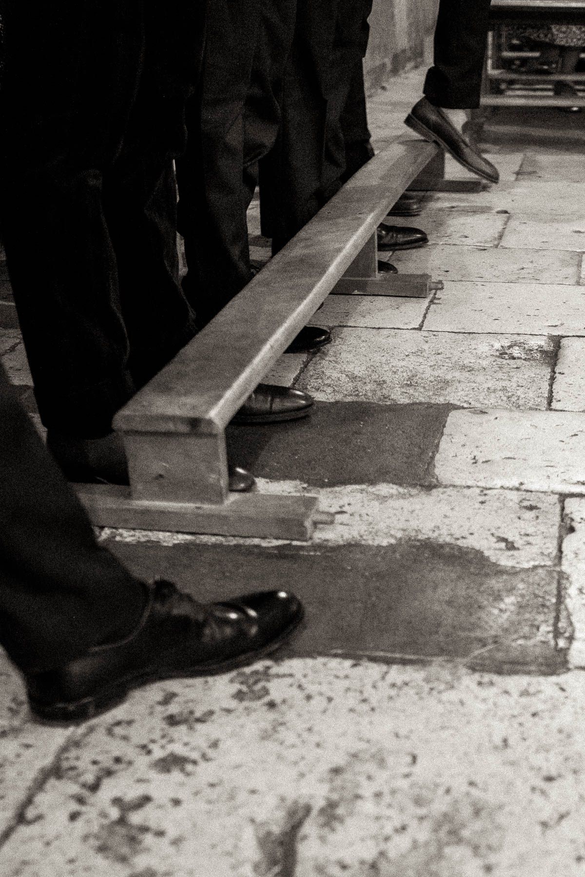 A series of black and white photographs showing dress shoes and pant legs walking on a stone floor.