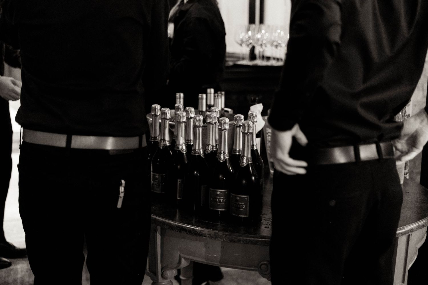 A black and white photo shows people gathered at a bar counter with bottles and glasses visible.