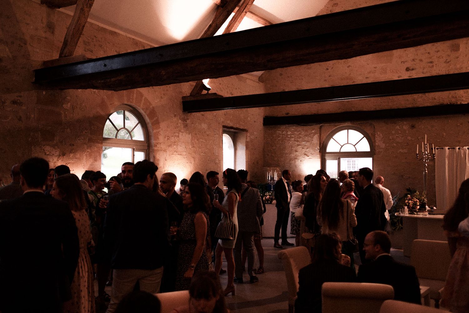 People gather inside a dimly lit historic brick building with exposed wooden beams and arched windows.