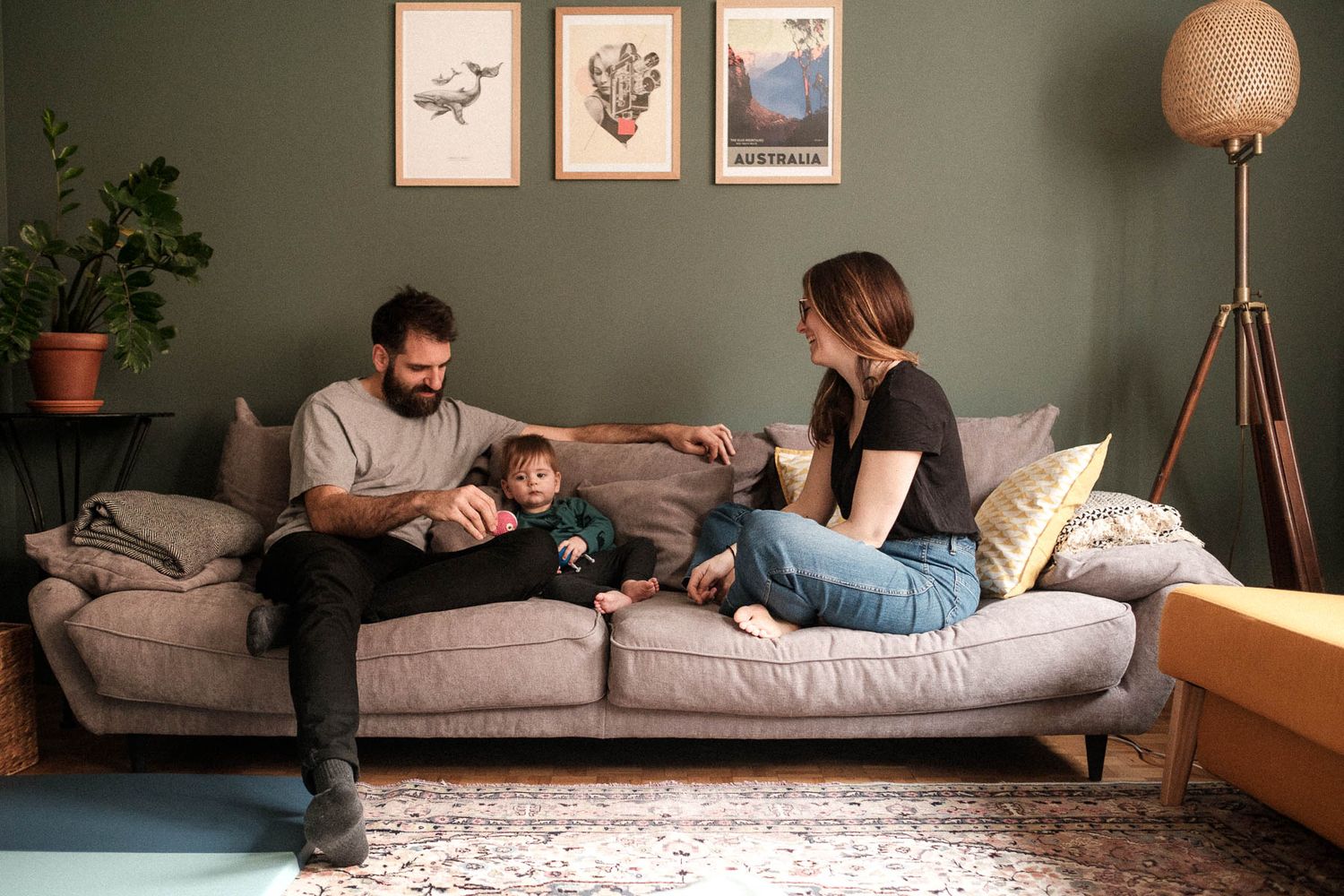 Couple relaxing together on a gray couch in a cozy living room with wall art and plants.