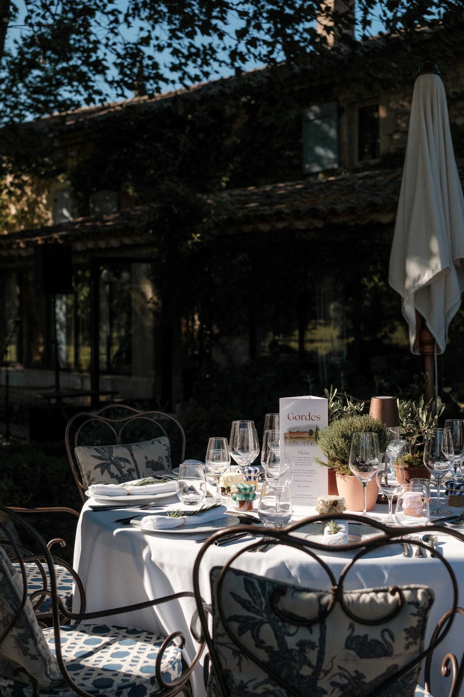 Elegant outdoor restaurant tables set with white linens and wine glasses cast dramatic shadows in natural sunlight.