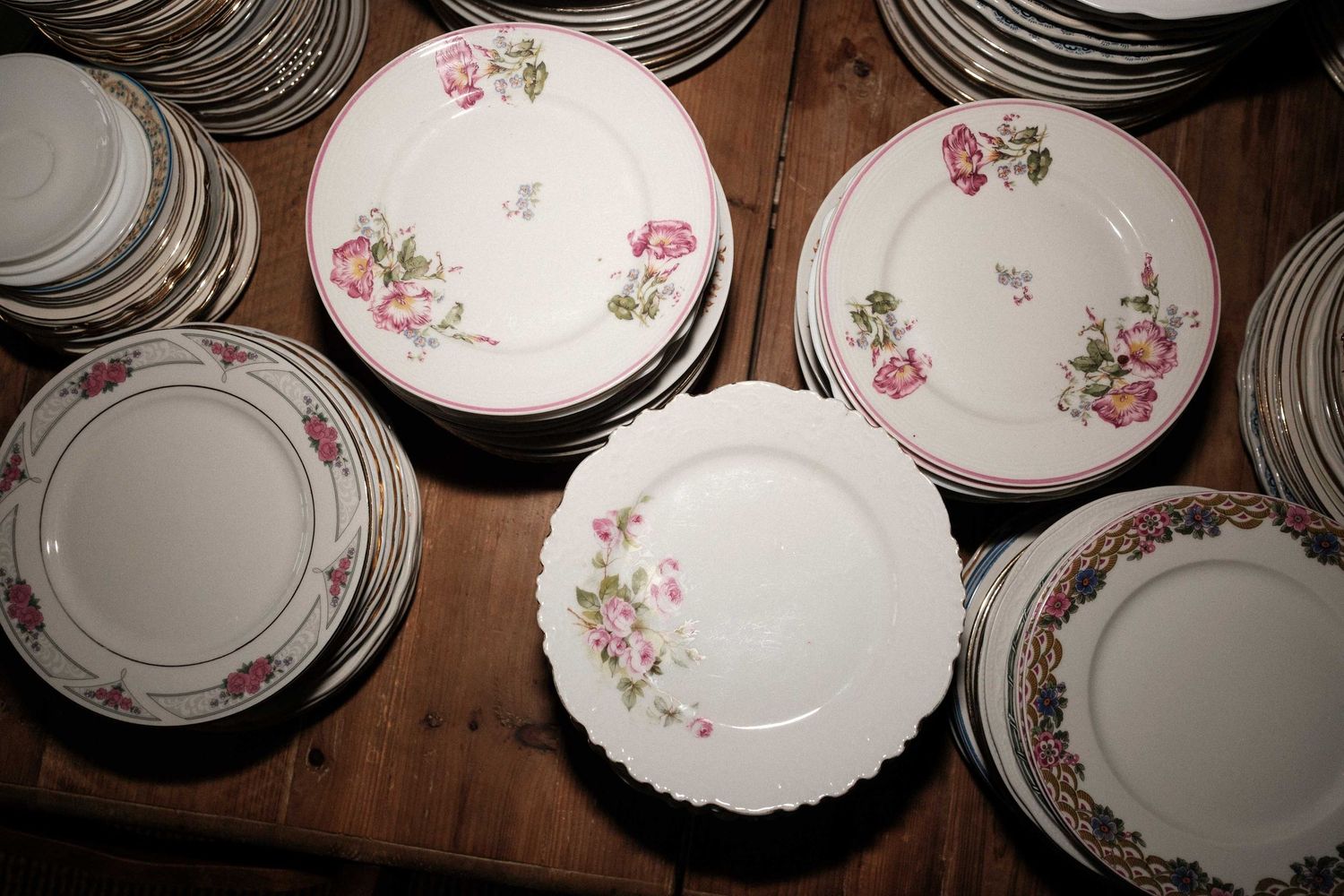 Vintage porcelain plates with delicate pink floral patterns arranged on a dark wooden surface.