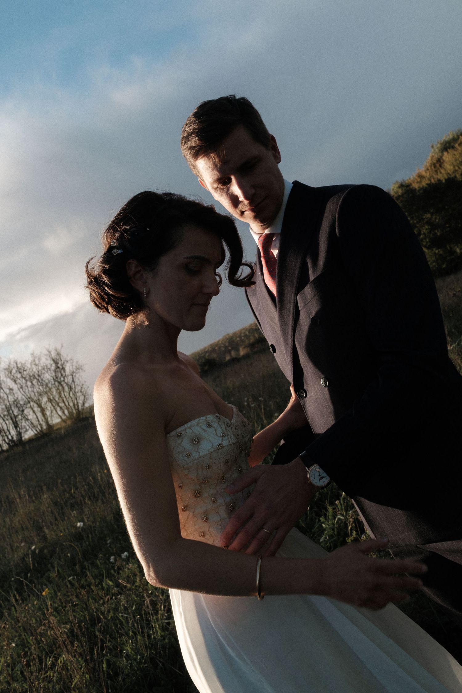 A romantic wedding couple embraces in a field during golden hour, captured in a series of intimate moments.