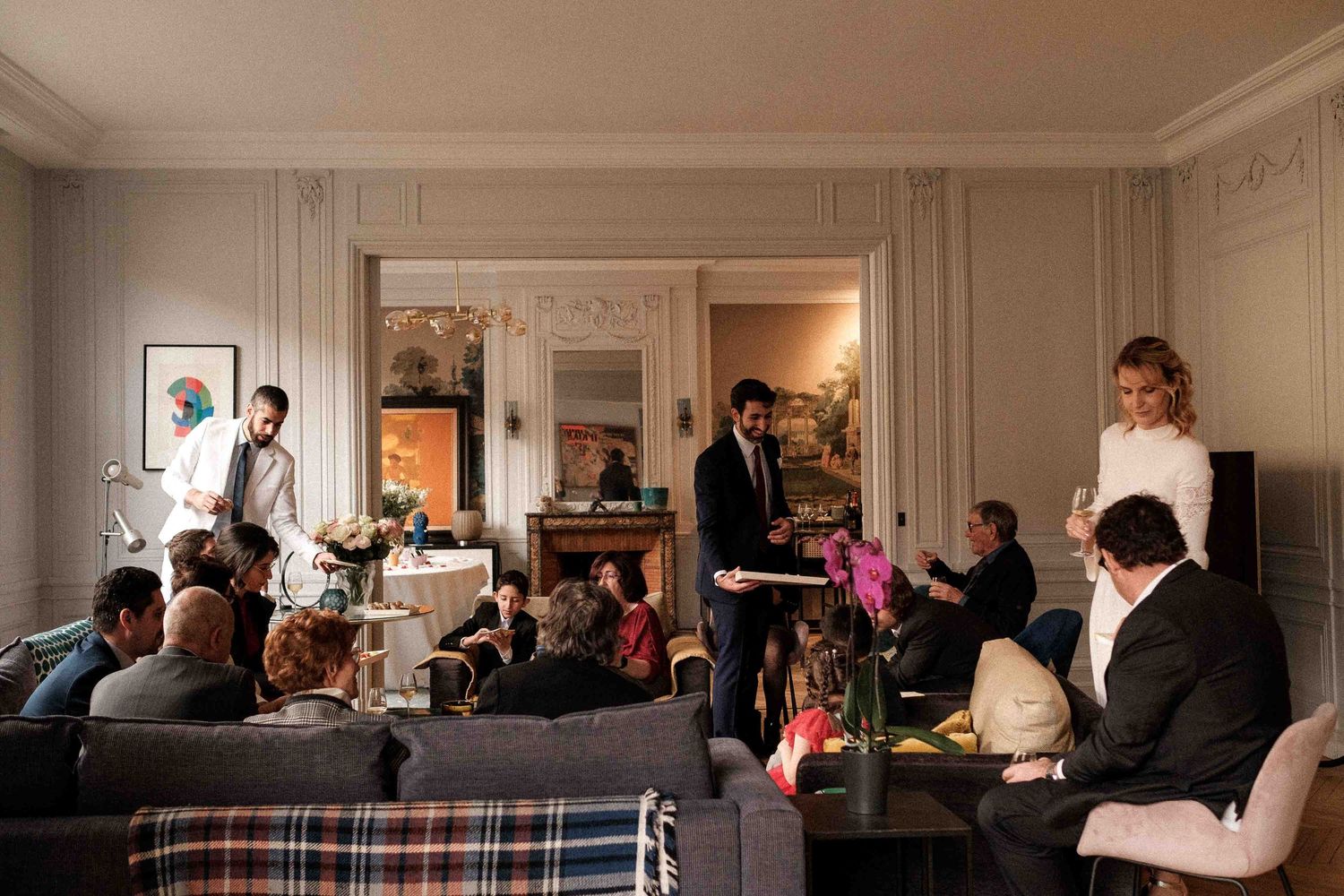 People gathered in an elegant living room for a social event with white molded walls and warm lighting.