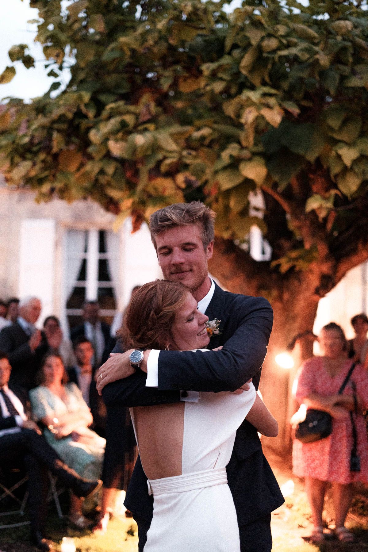 A couple shares a romantic dance moment under tree foliage at an outdoor wedding reception.