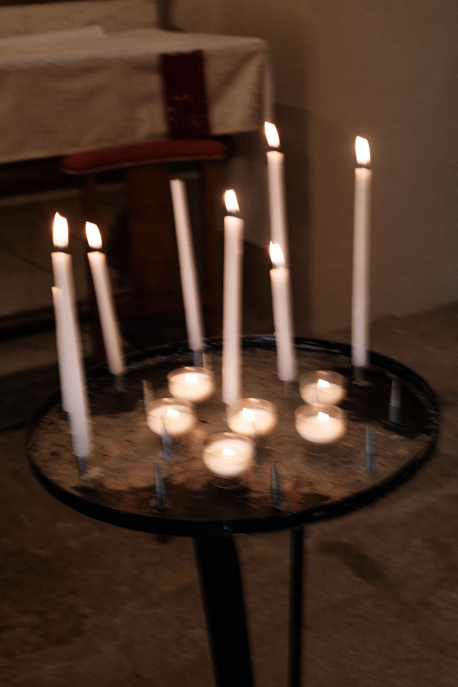 Multiple white candles arranged on a dark circular surface glow softly in a dimly lit setting.