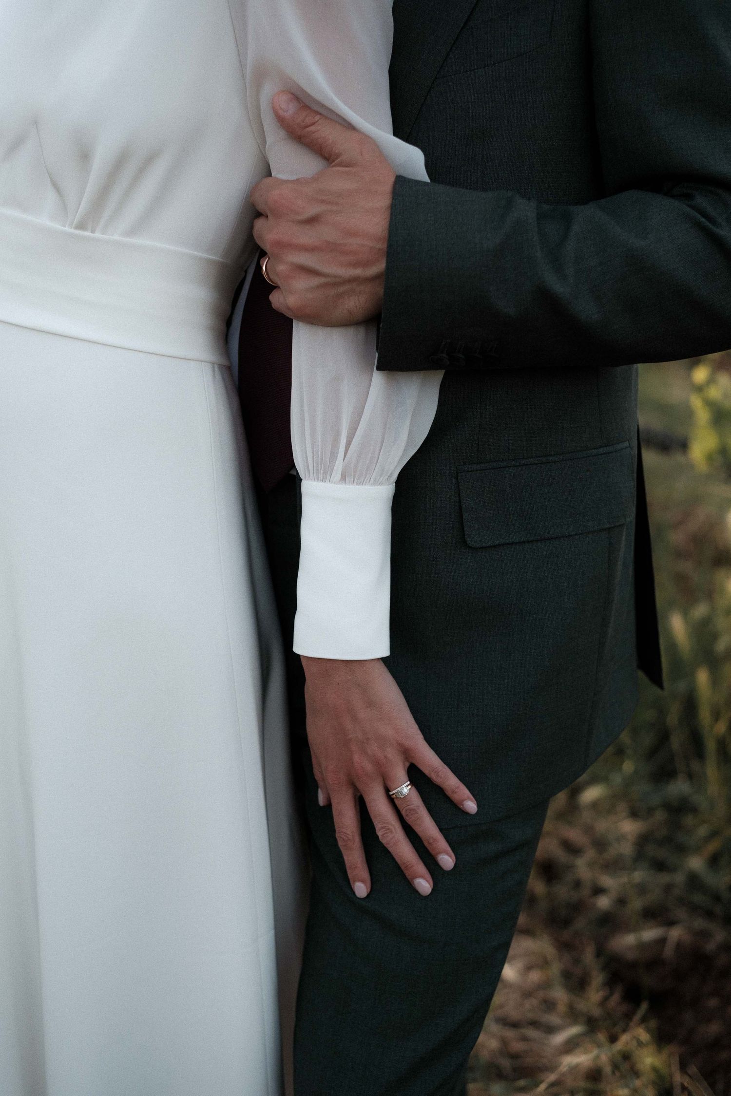 Close-up details of a bride in white dress and groom in black suit embracing during a wedding photoshoot.