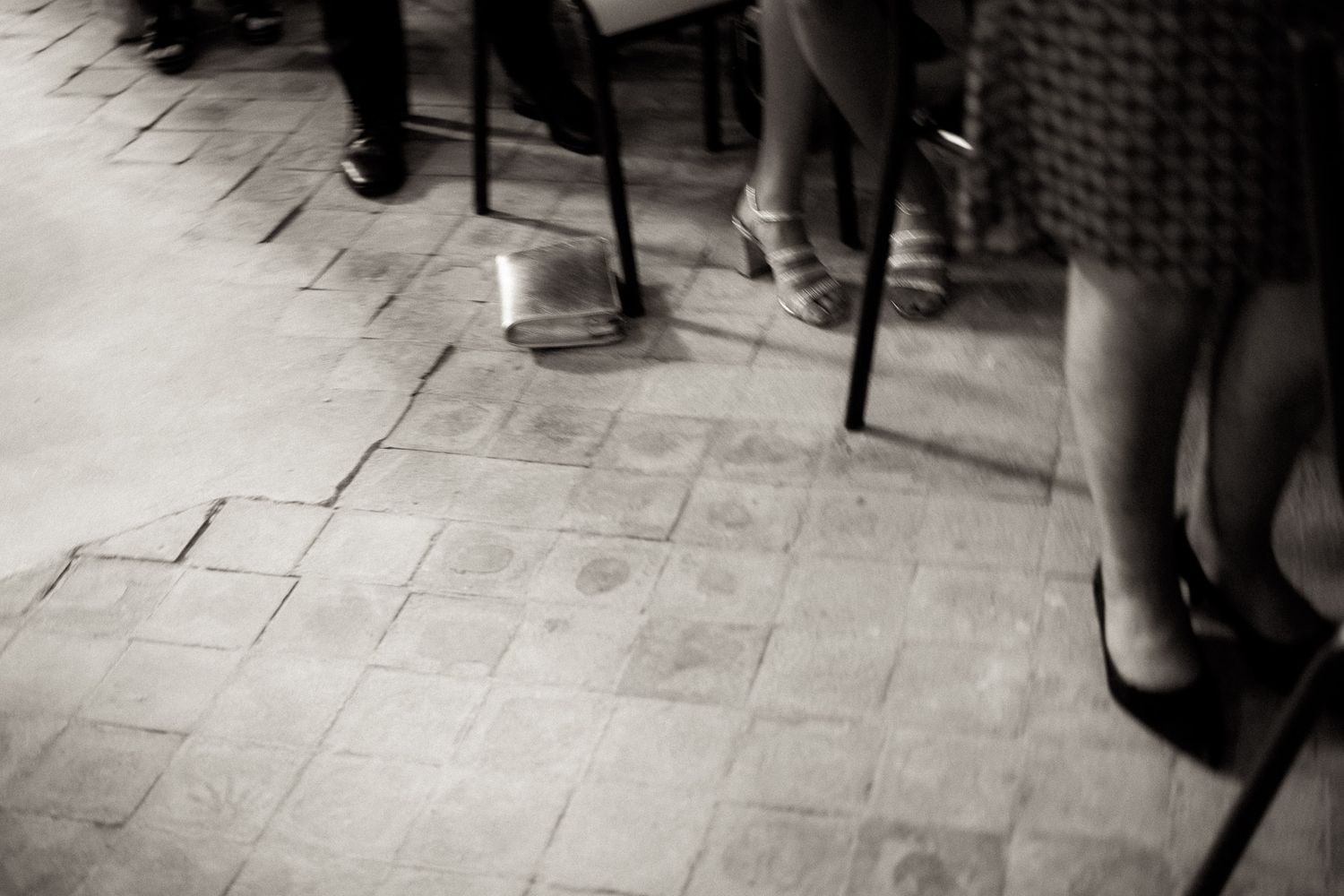 Black and white image of people's feet walking on a stone floor in formal attire.