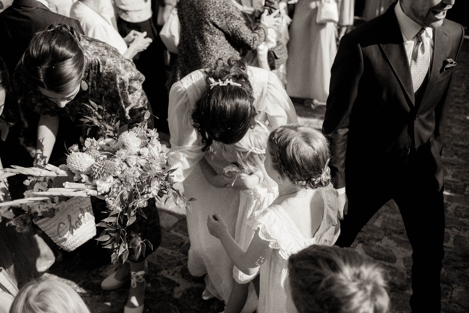 Wedding guests gather in a reception hall sharing intimate conversations and embraces in black and white photography.
