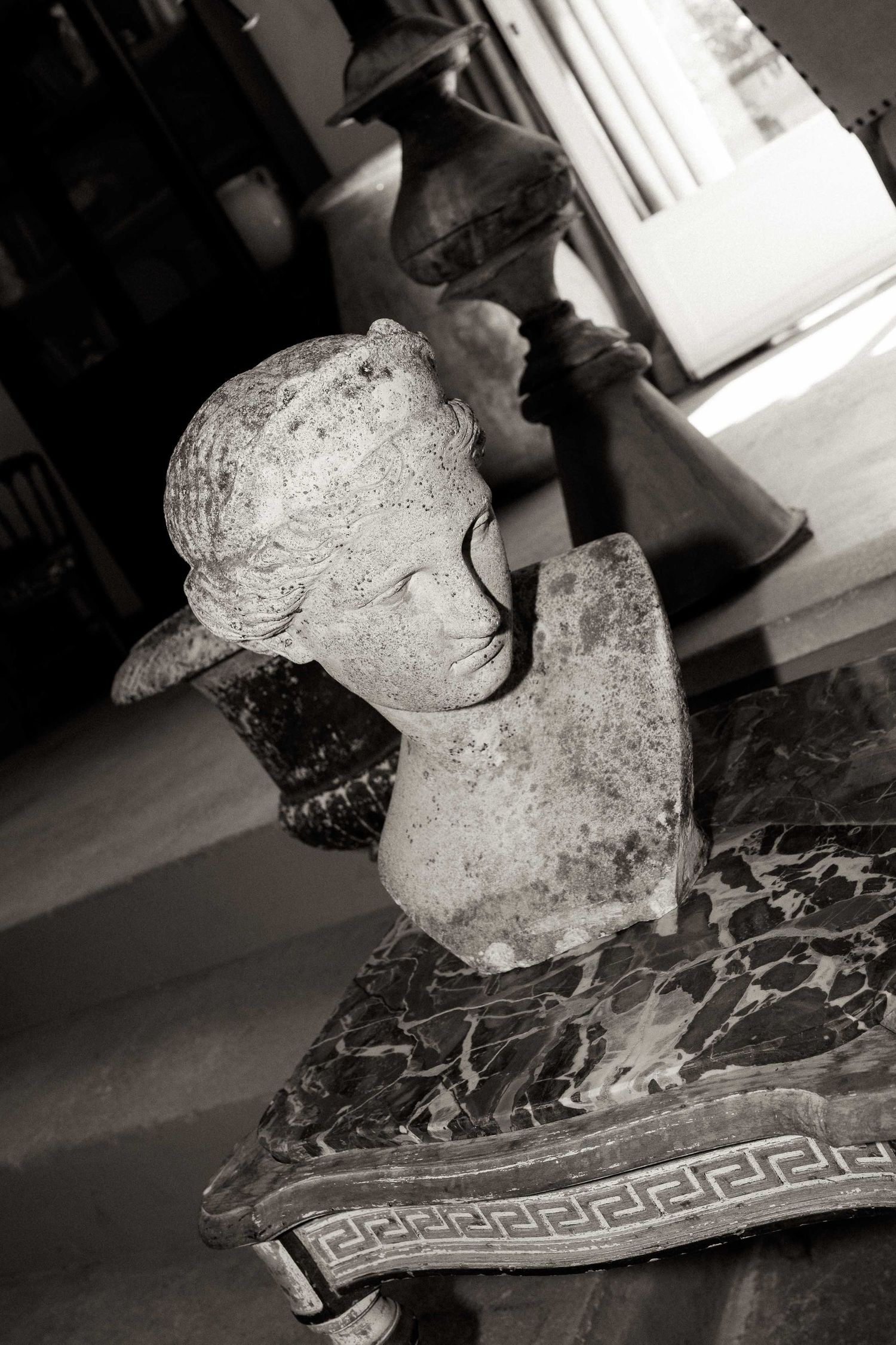 Weathered stone sculpture on a decorative marble base with Greek key pattern design.