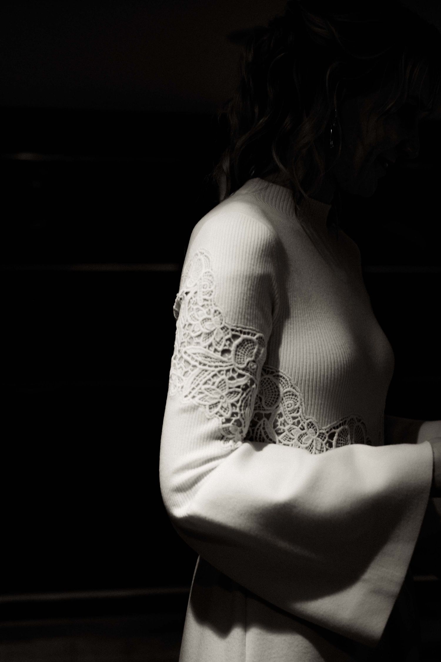 White lace details on fabric shown in dramatic black and white lighting creating an intimate mood.