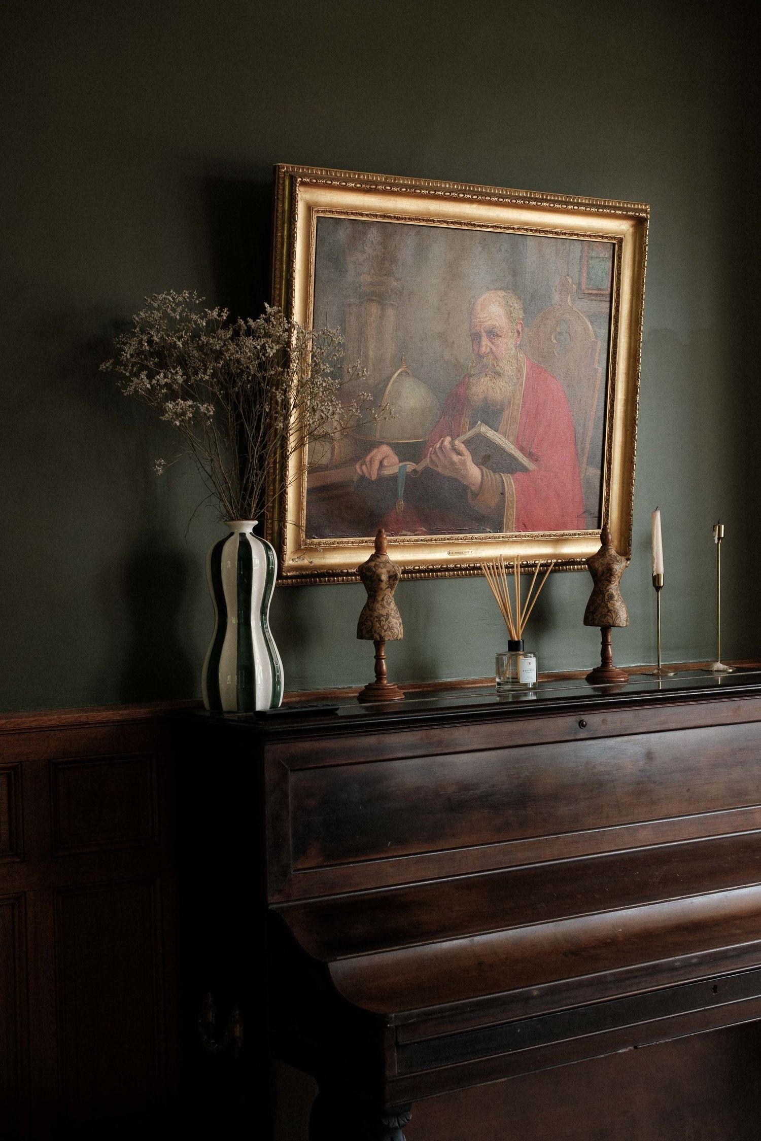 Dark moody shot of a wooden piano with gold-framed artwork and decorative vases arranged on top.